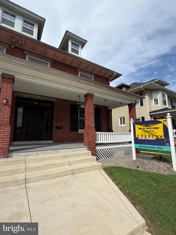 Red-brick home with a covered porch, wide concrete steps, and a yellow moving sign by the lawn.