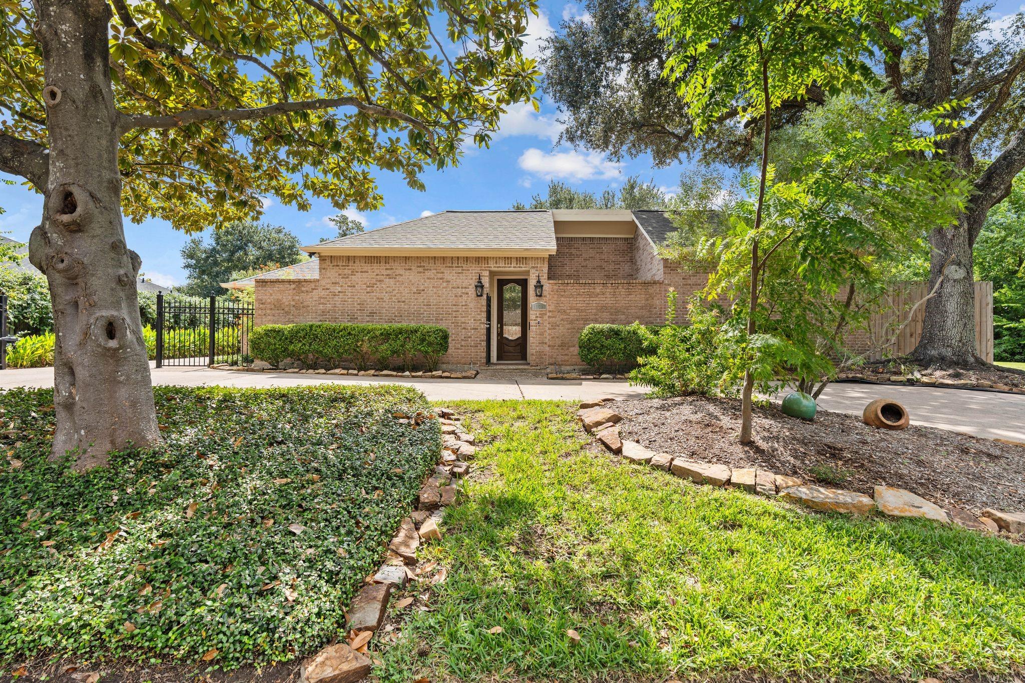 Brick home with a dark front door, mature trees, and a landscaped front yard.