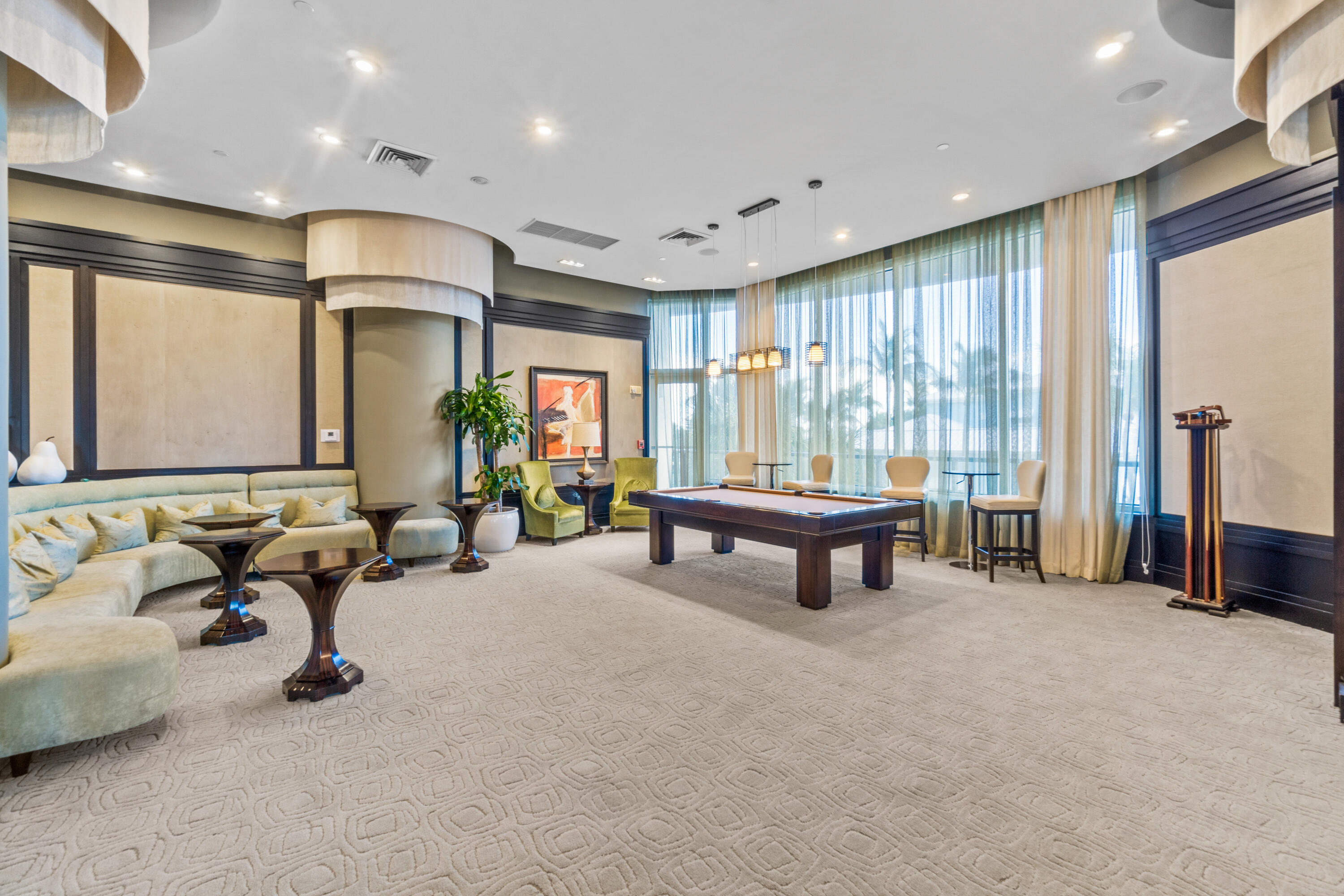 Billiards lounge with a dark wood pool table, curved cream sectional, and tall curtained windows.