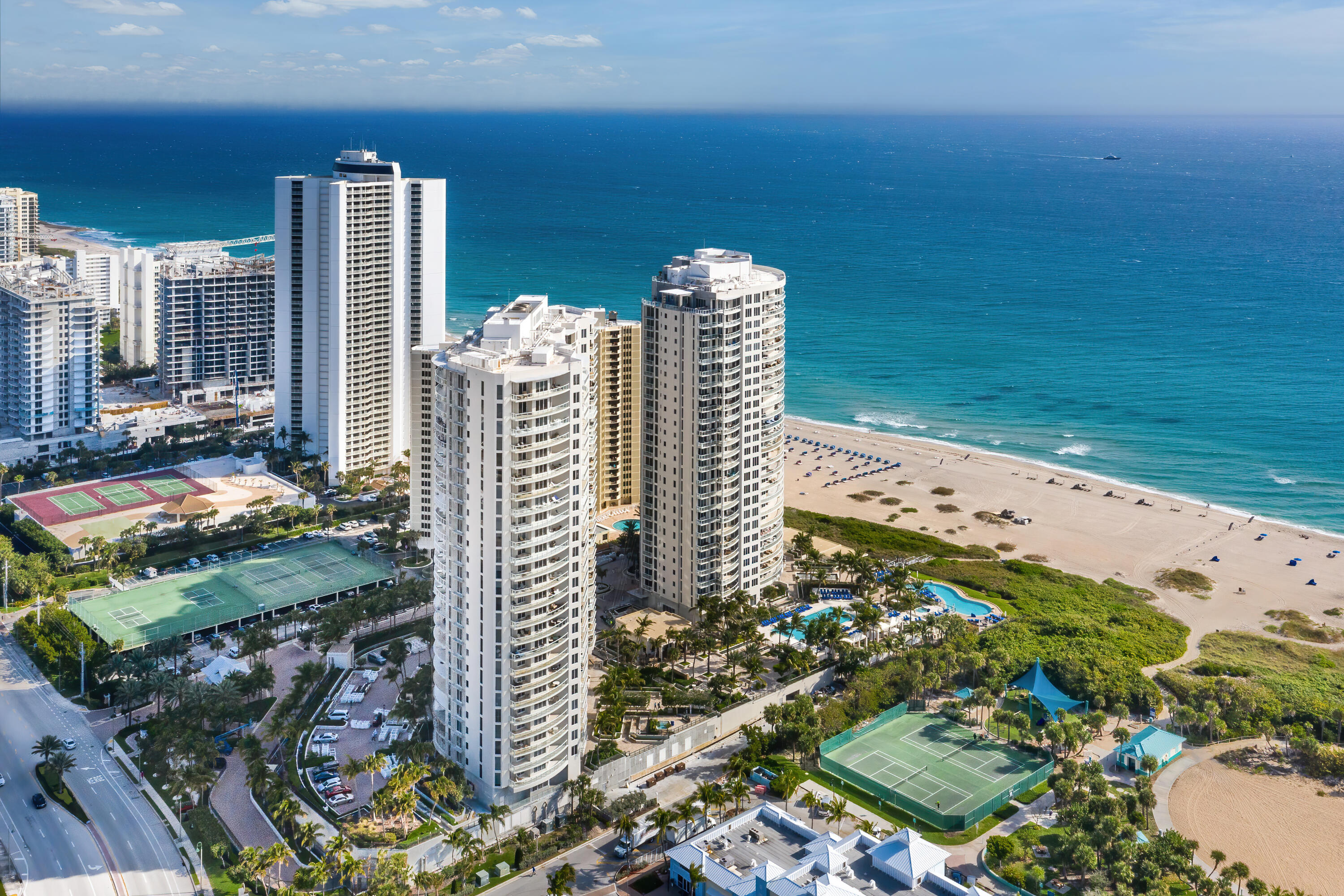 Oceanfront condominium towers beside a sandy beach, with pools and tennis courts.