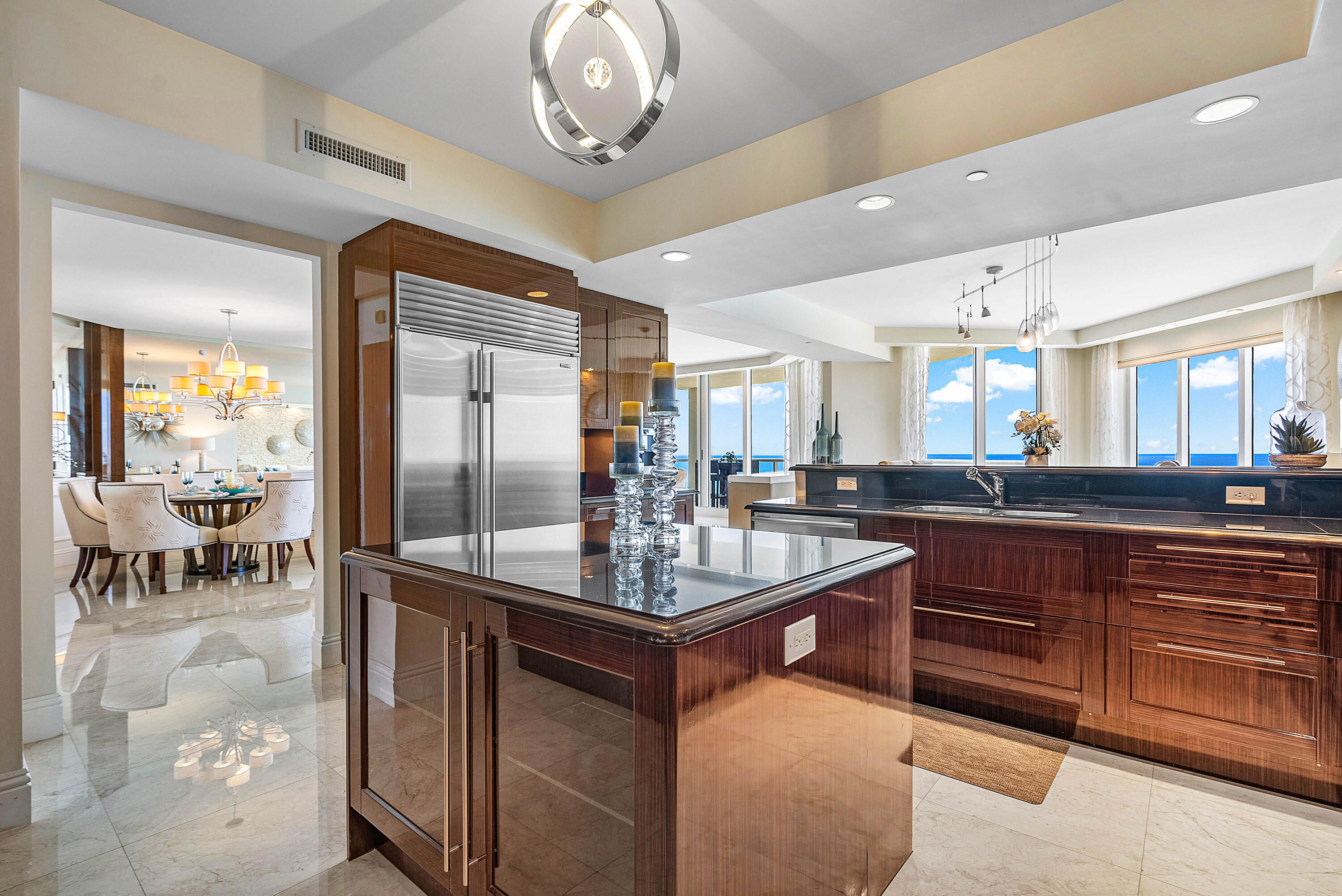 Condo kitchen with dark wood cabinets, a large island, stainless appliances, and ocean views through floor-to-ceiling windows.