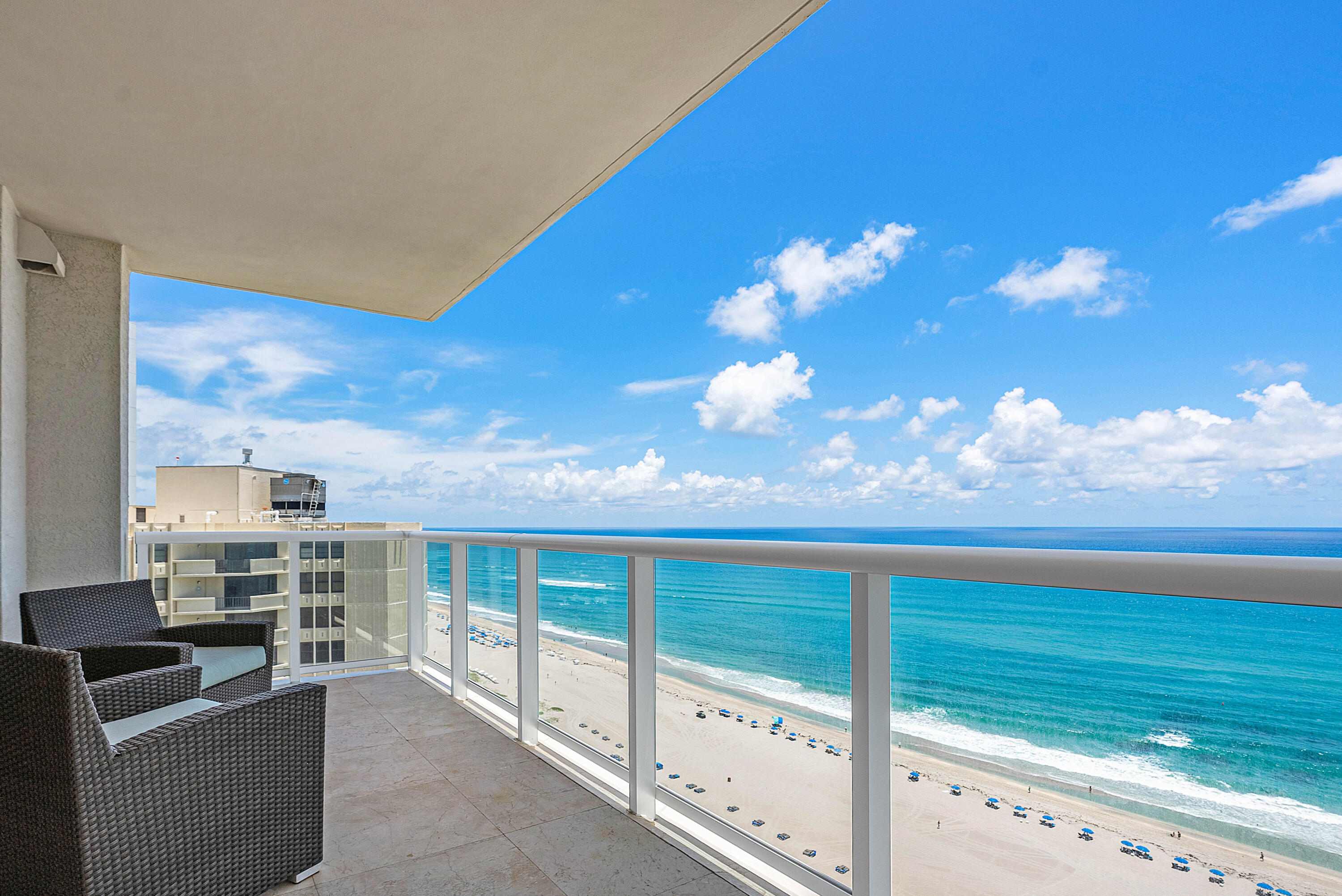 Oceanfront balcony with wicker chairs overlooking a sandy beach and turquoise water.