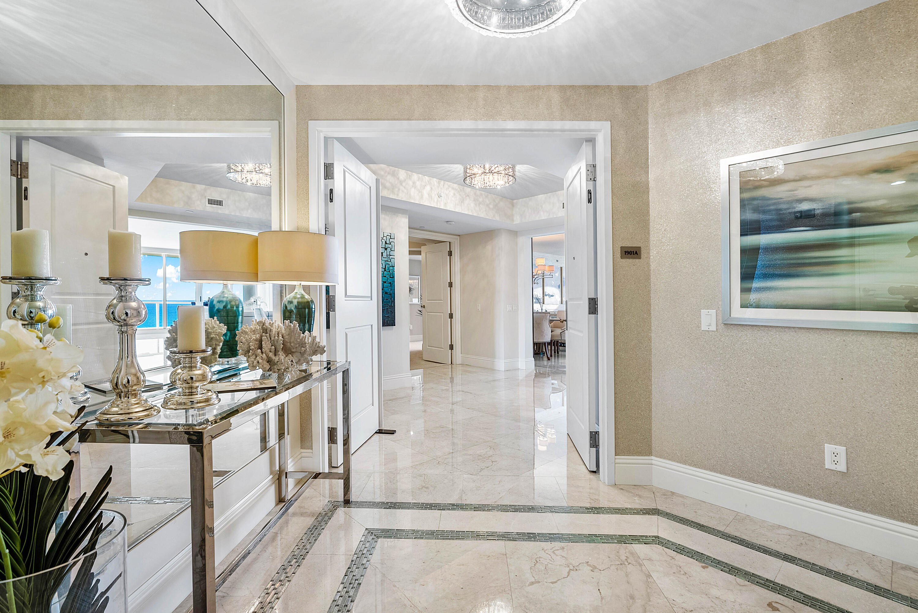 Condominium entry foyer with polished marble floors, a mirrored console table, and ocean visible through an adjoining room.