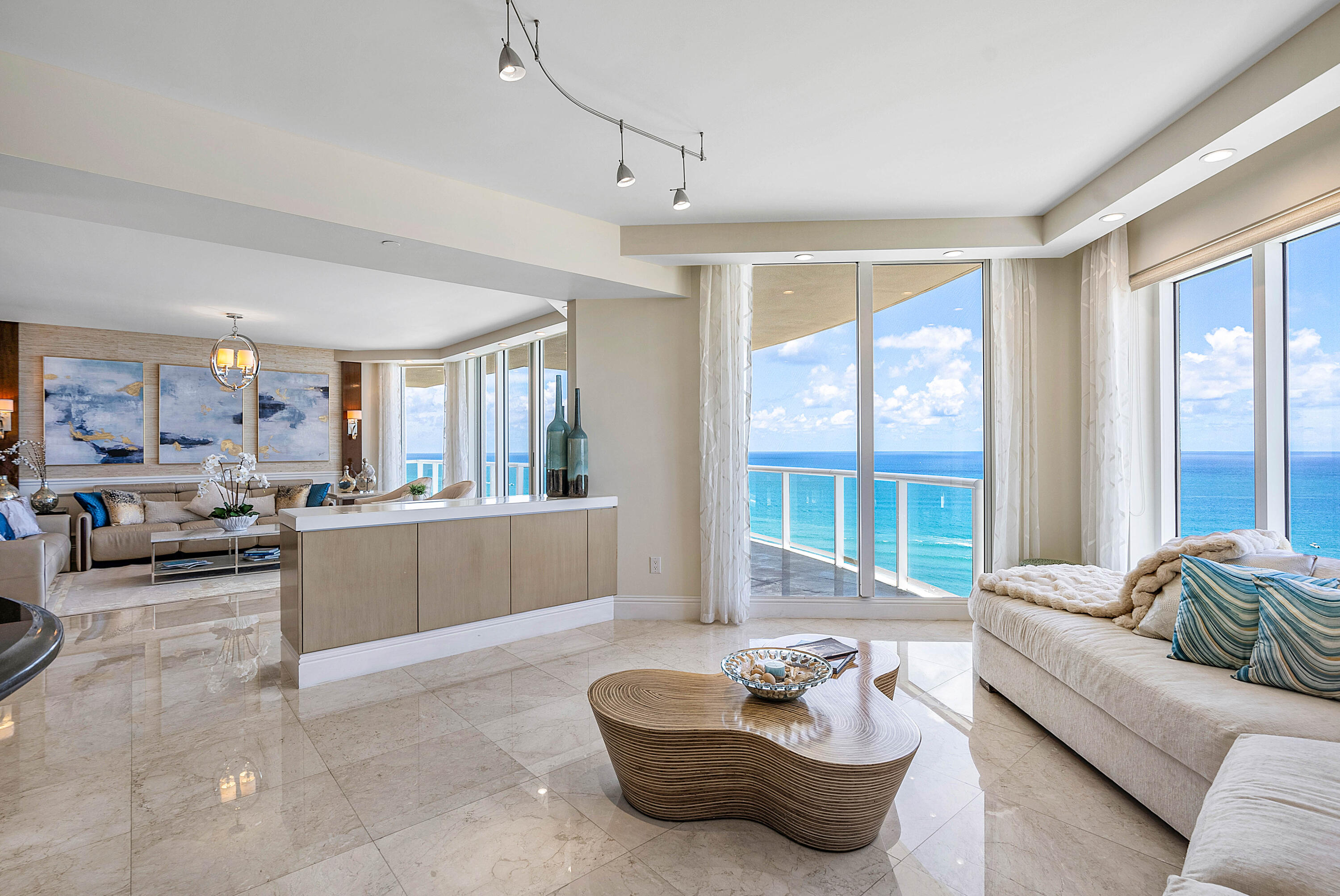 Oceanfront condo living room with floor-to-ceiling windows, a balcony, and sweeping ocean views.