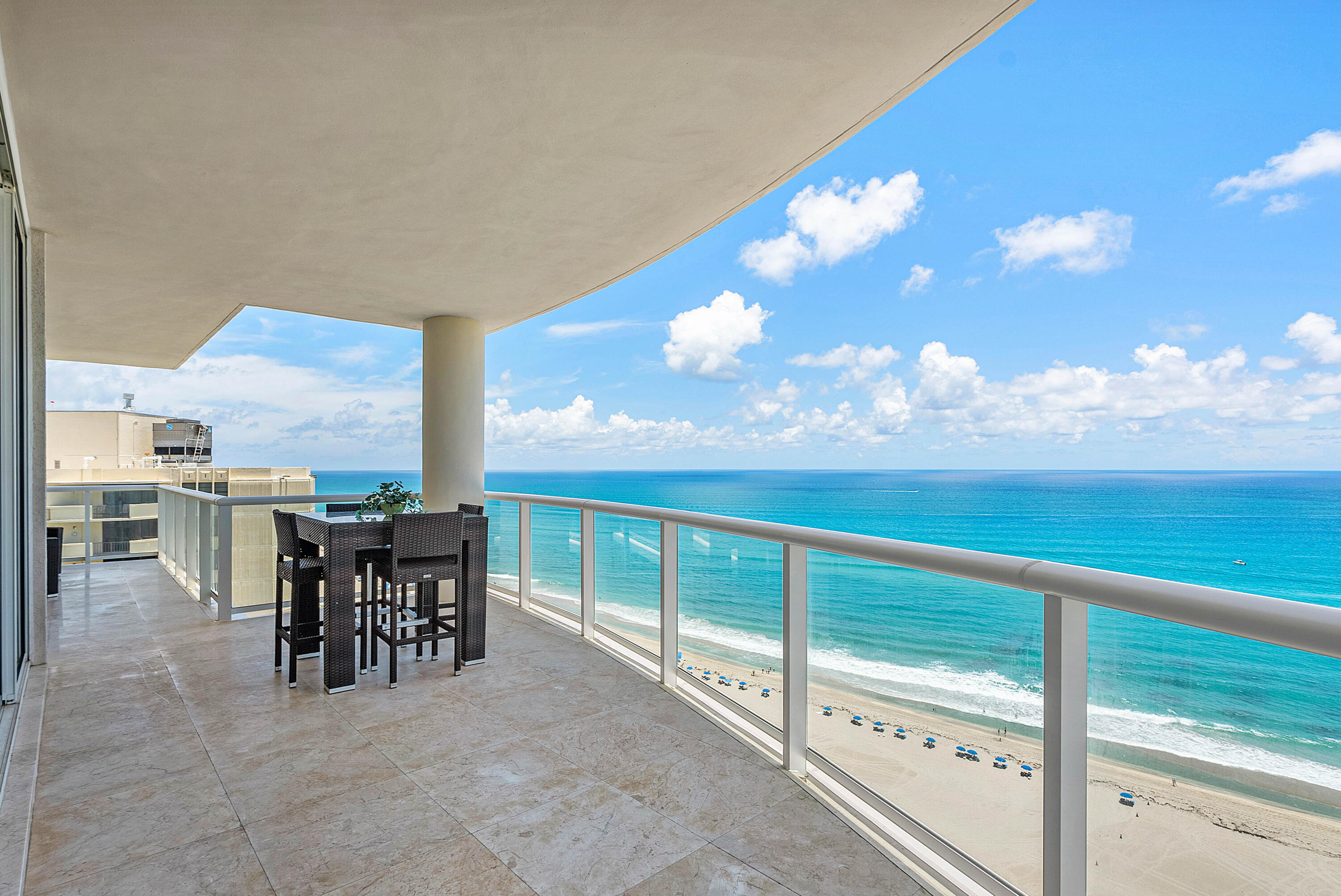 Oceanfront condo balcony with outdoor dining set overlooking a sandy beach and turquoise water.