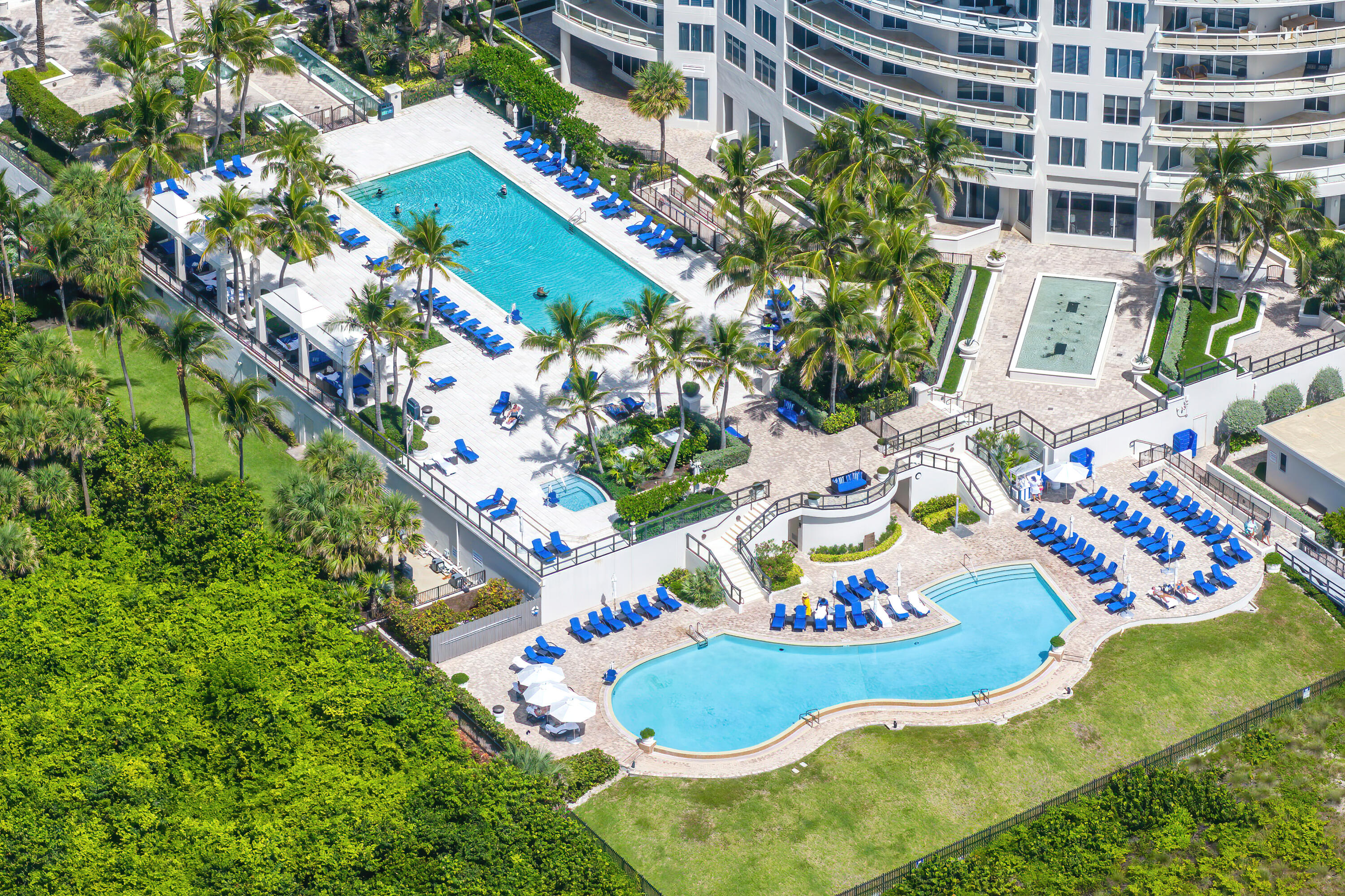 Aerial view of a condominium pool deck with two pools, blue loungers, and palm trees.