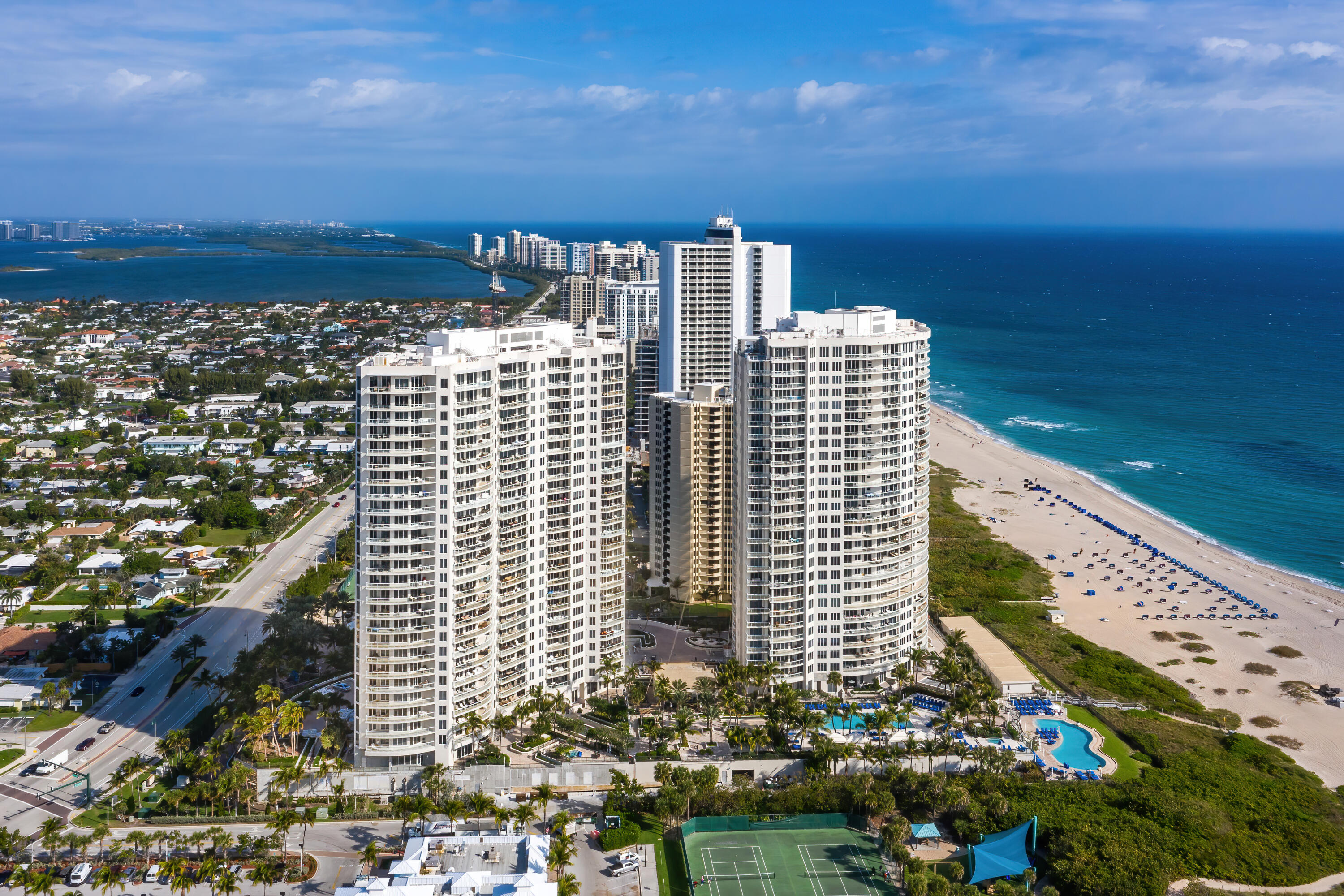Aerial view of oceanfront condominium towers, beach, pools and tennis court.