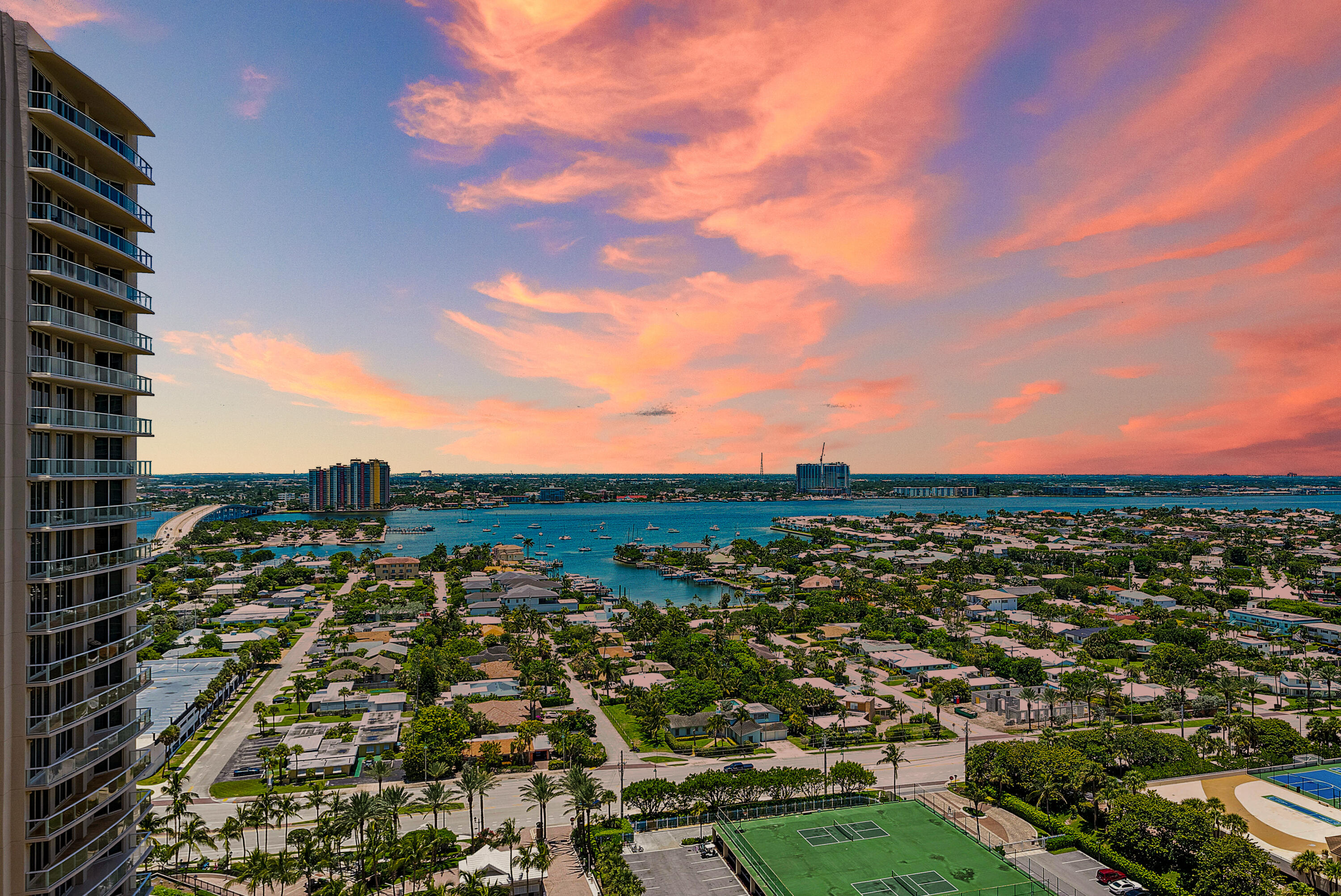 High-rise waterfront view over a marina channel and neighborhood beneath vivid pink sunset clouds.