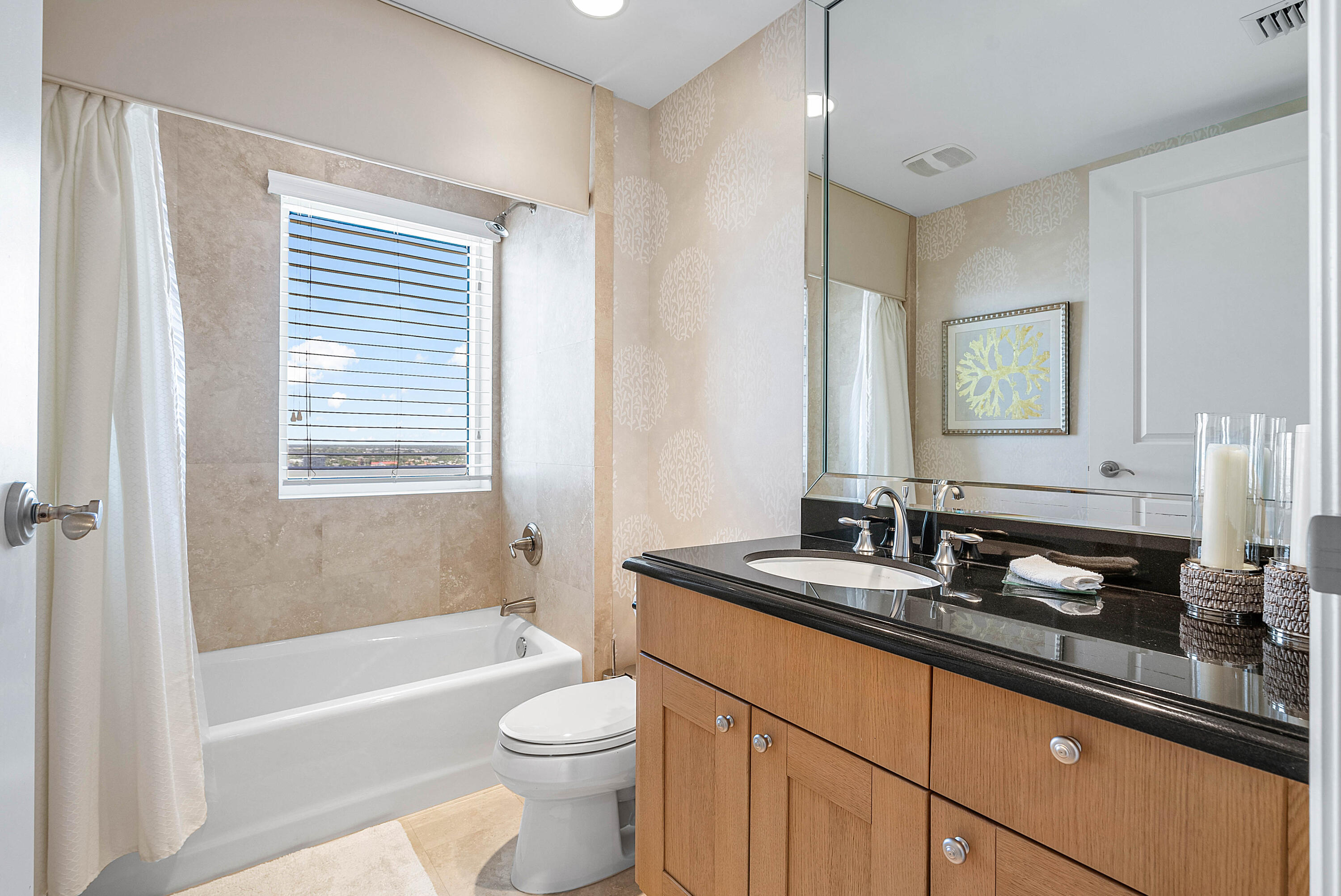 Bathroom with a tub, window blinds, toilet, and wood vanity with a black countertop.