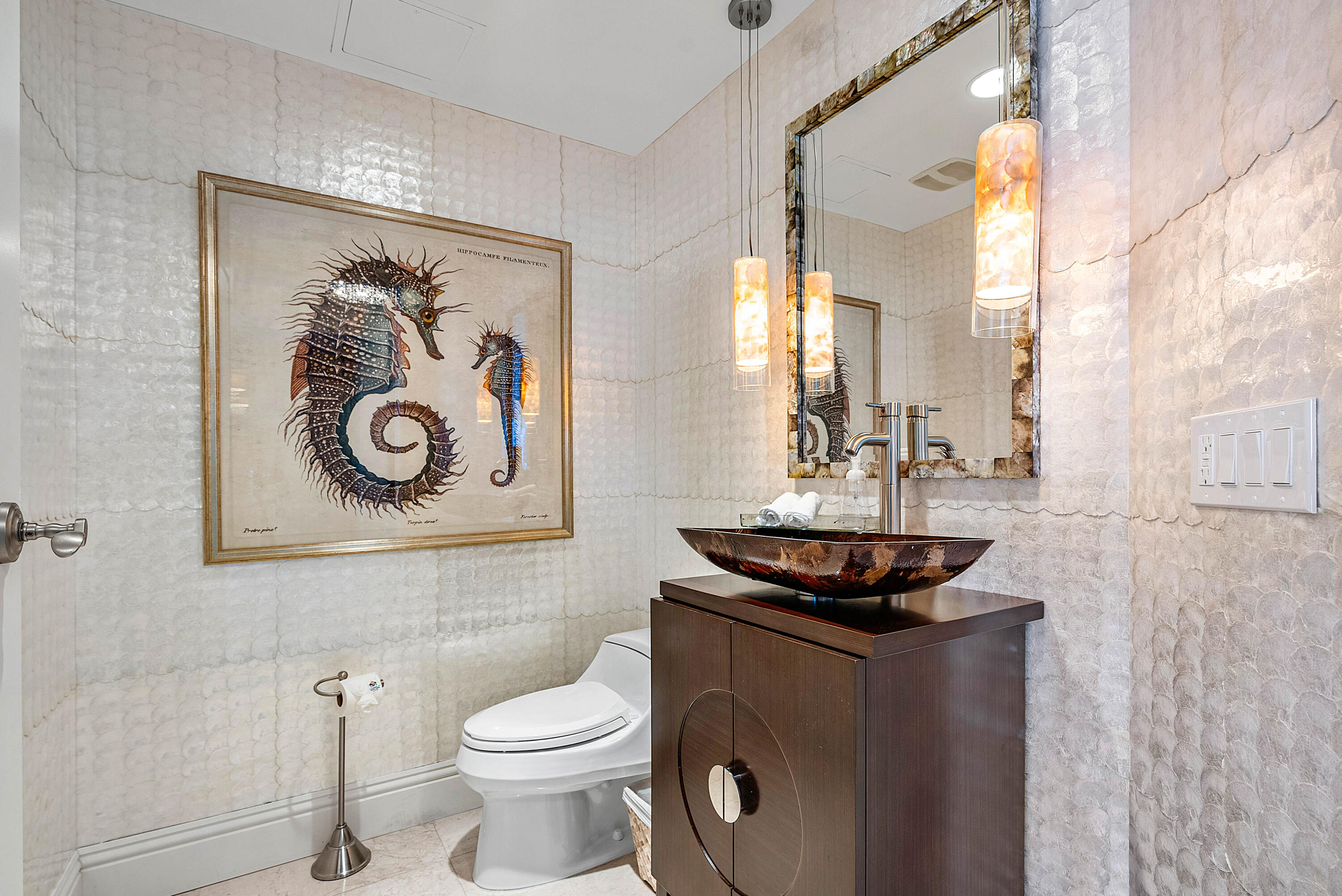 Powder room with a dark vessel sink, framed seahorse artwork, and glowing pendant lights.