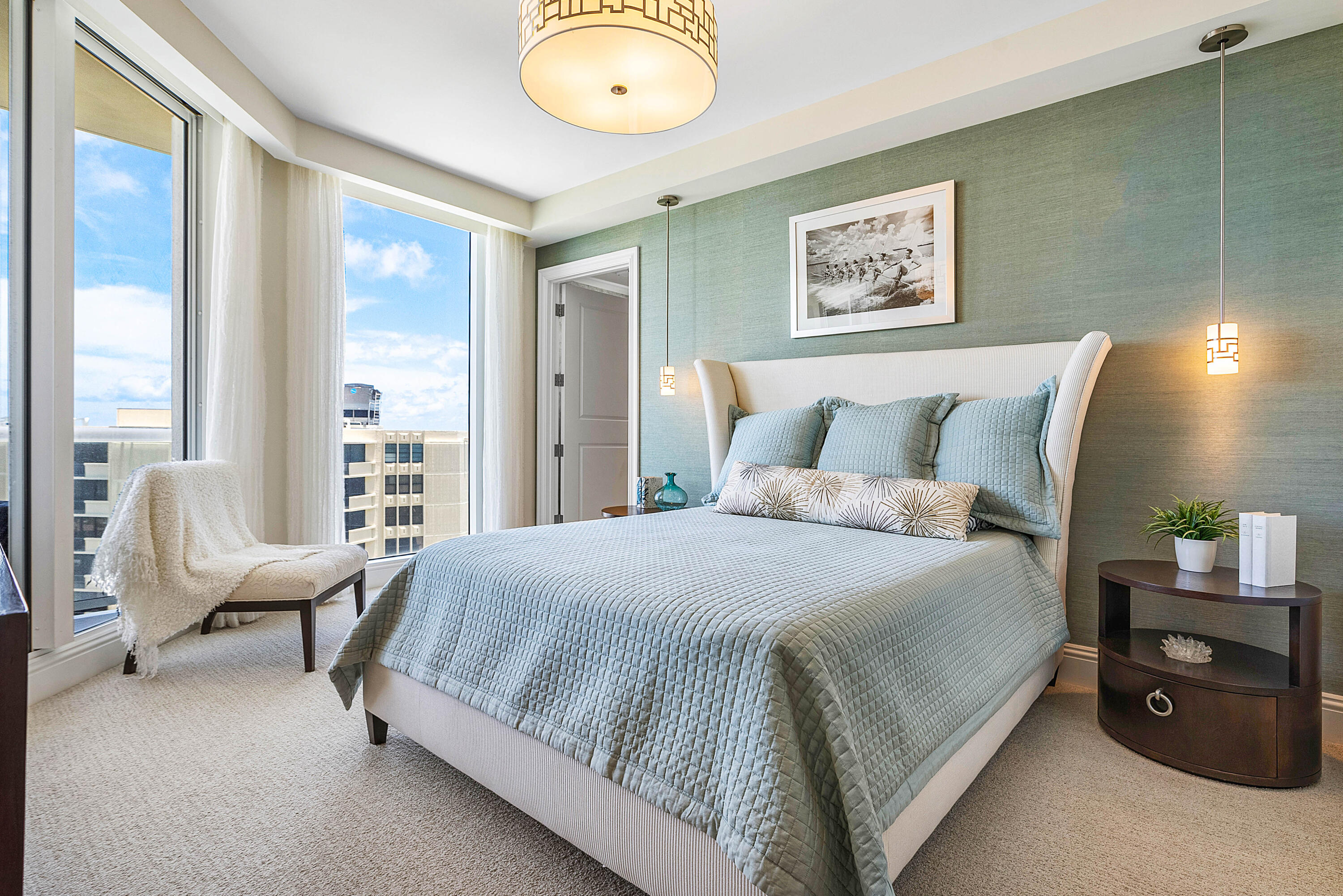 Bedroom with pale blue bedding, sage-green accent wall, and floor-to-ceiling windows.