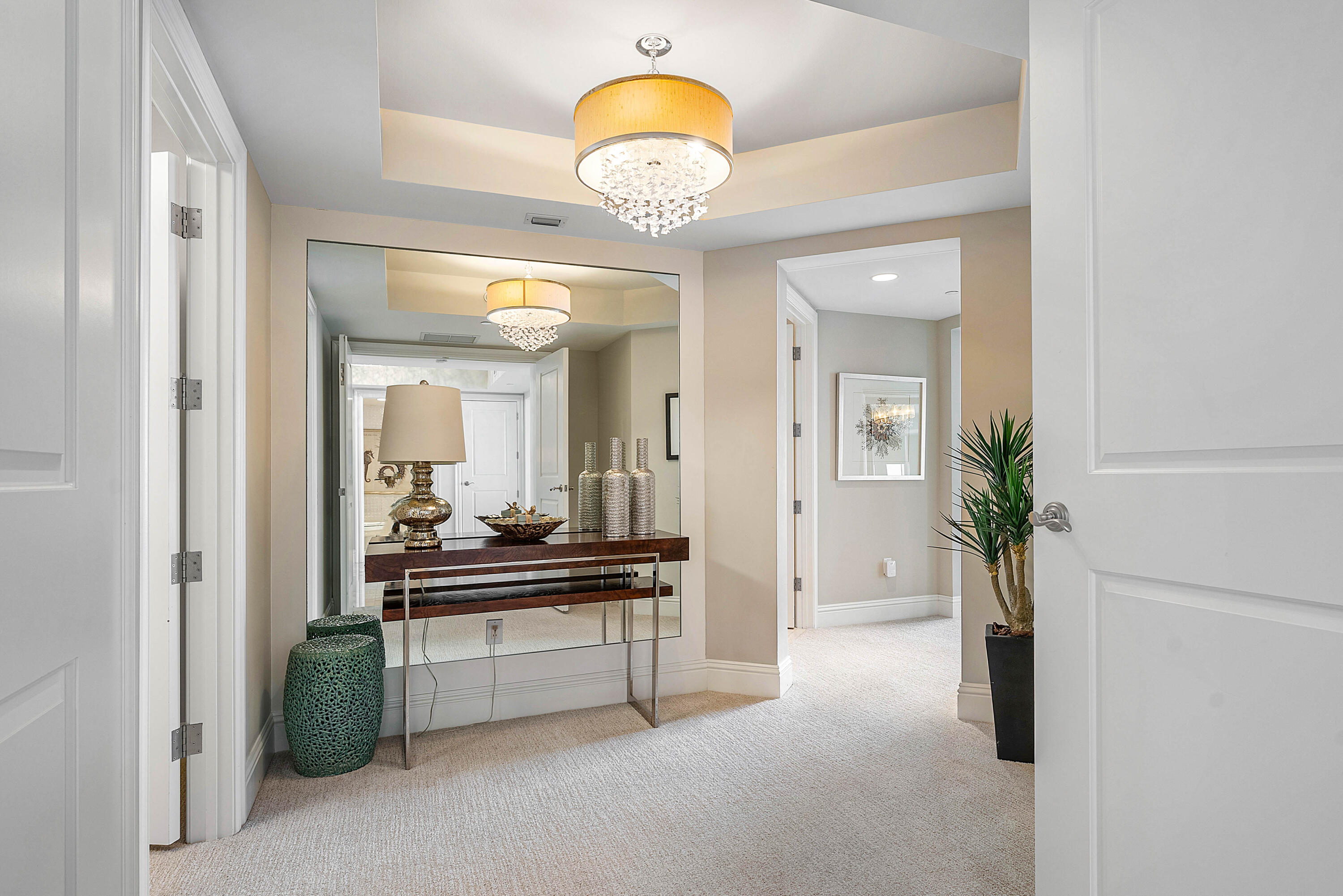 Condo foyer with mirrored console table, crystal chandelier, green stools, and potted plant.