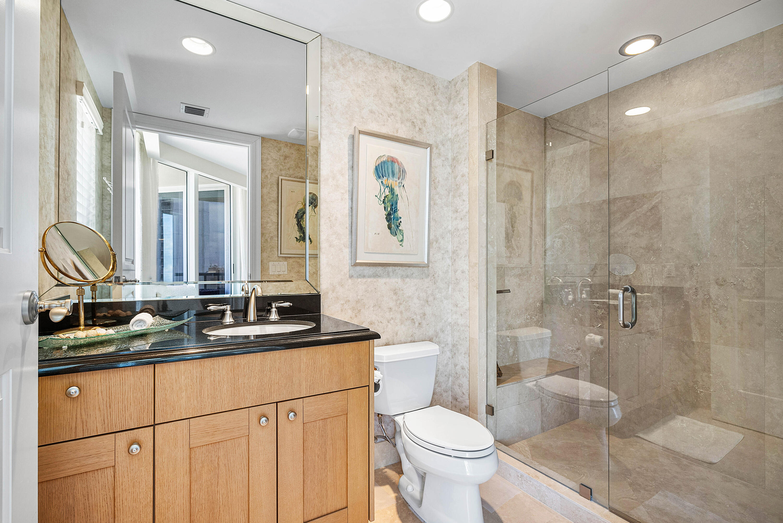 Bathroom with a wood vanity, black countertop, and glass-enclosed tiled shower.