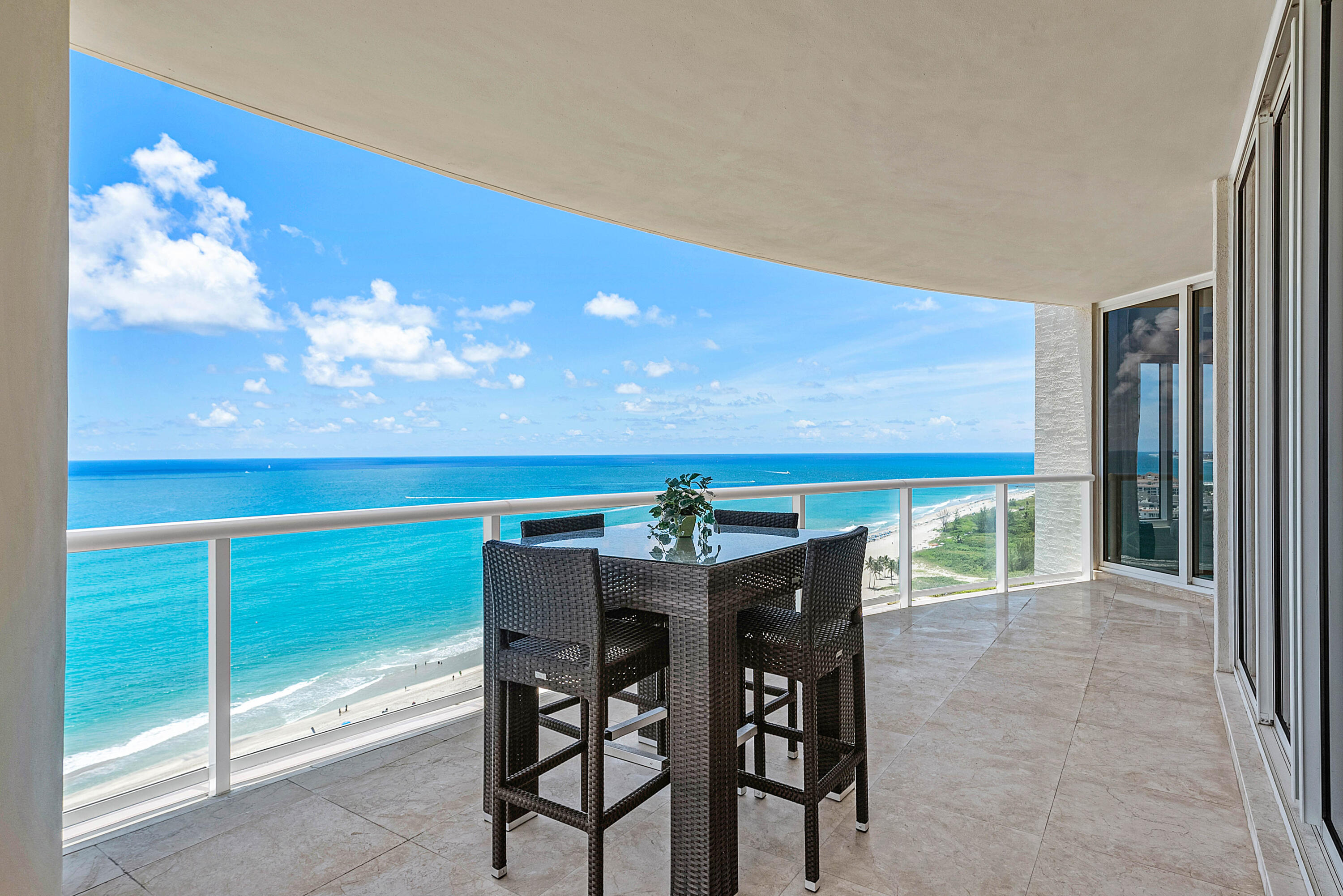 Oceanfront condo balcony with woven dining set and sweeping beach views.