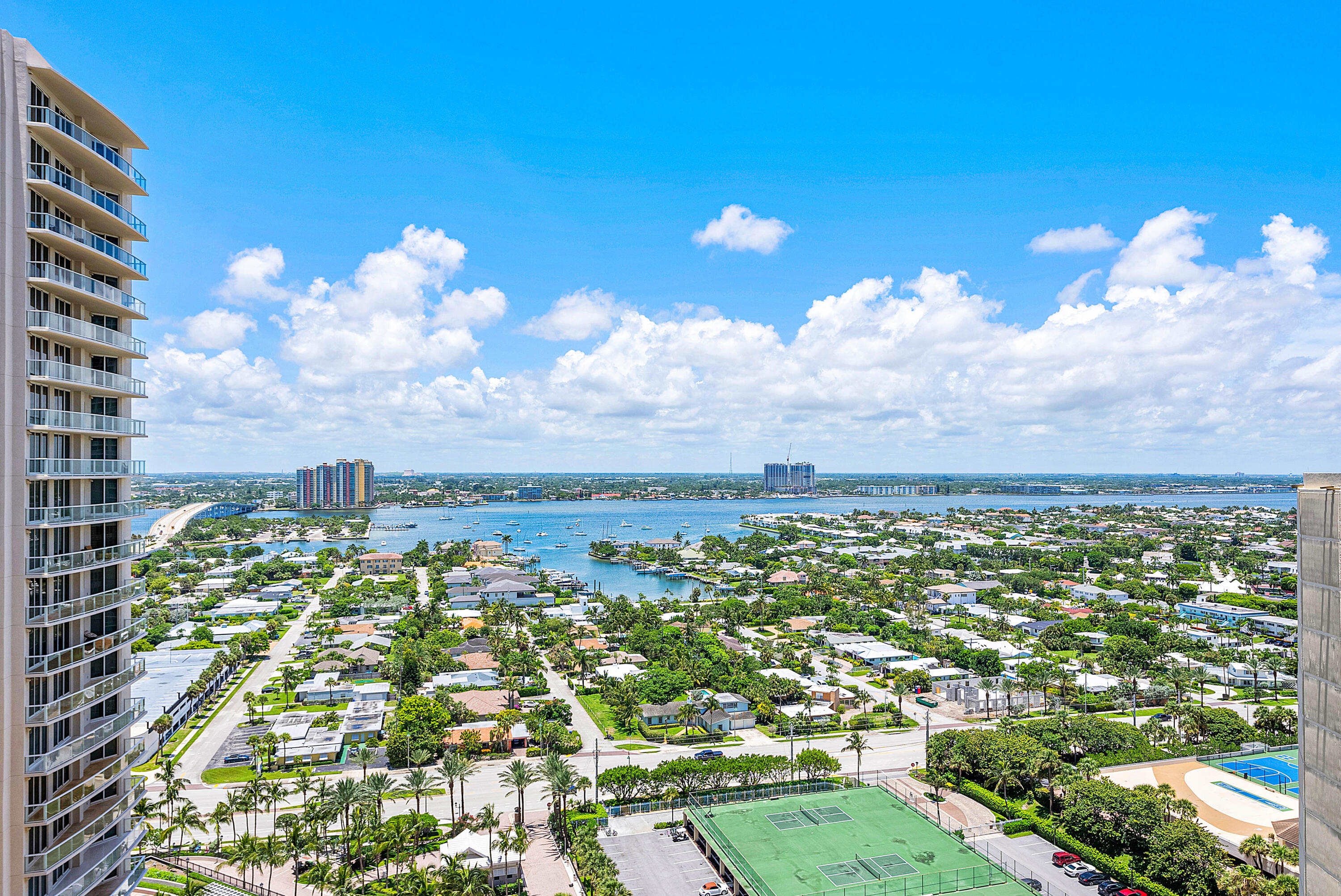 Waterfront view from a high-rise, with a bridge, neighborhood, and tennis courts below.