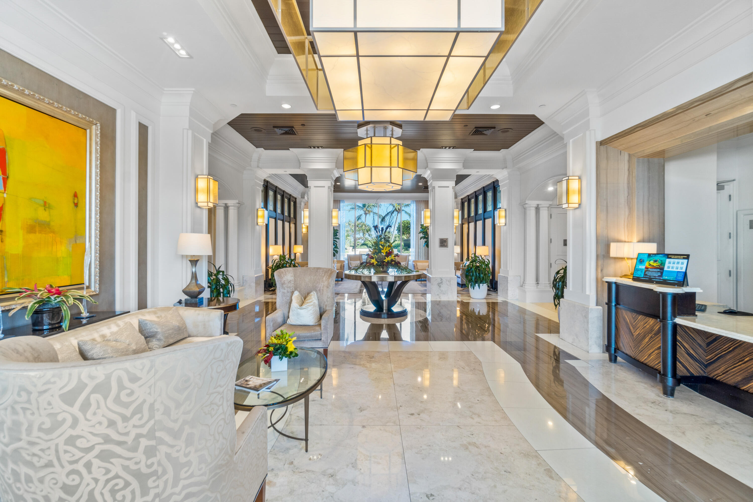 Condominium lobby with polished marble floors, lounge seating, white columns, and large chandeliers.