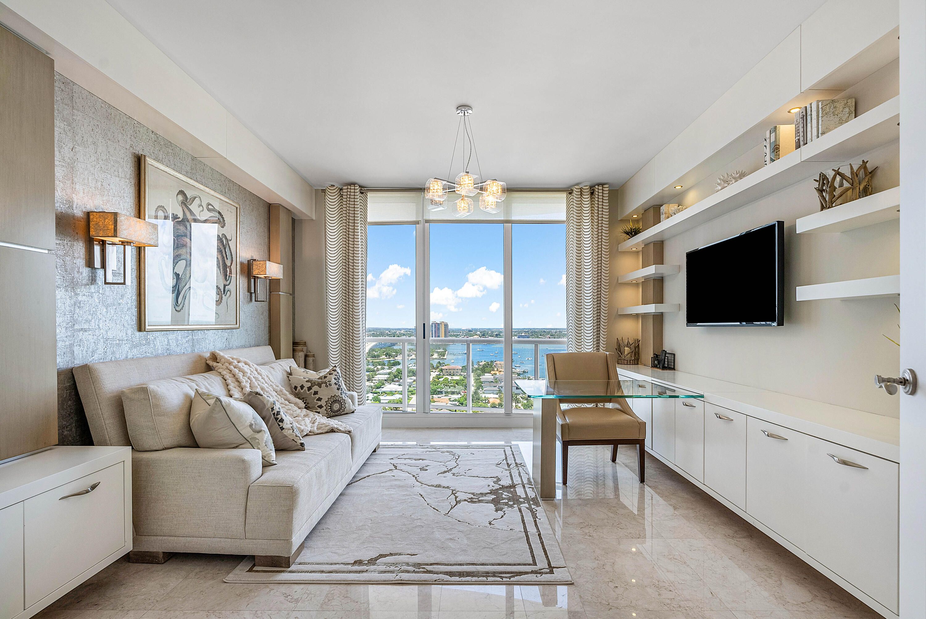 Furnished condo living room with floor-to-ceiling windows overlooking water and boats.