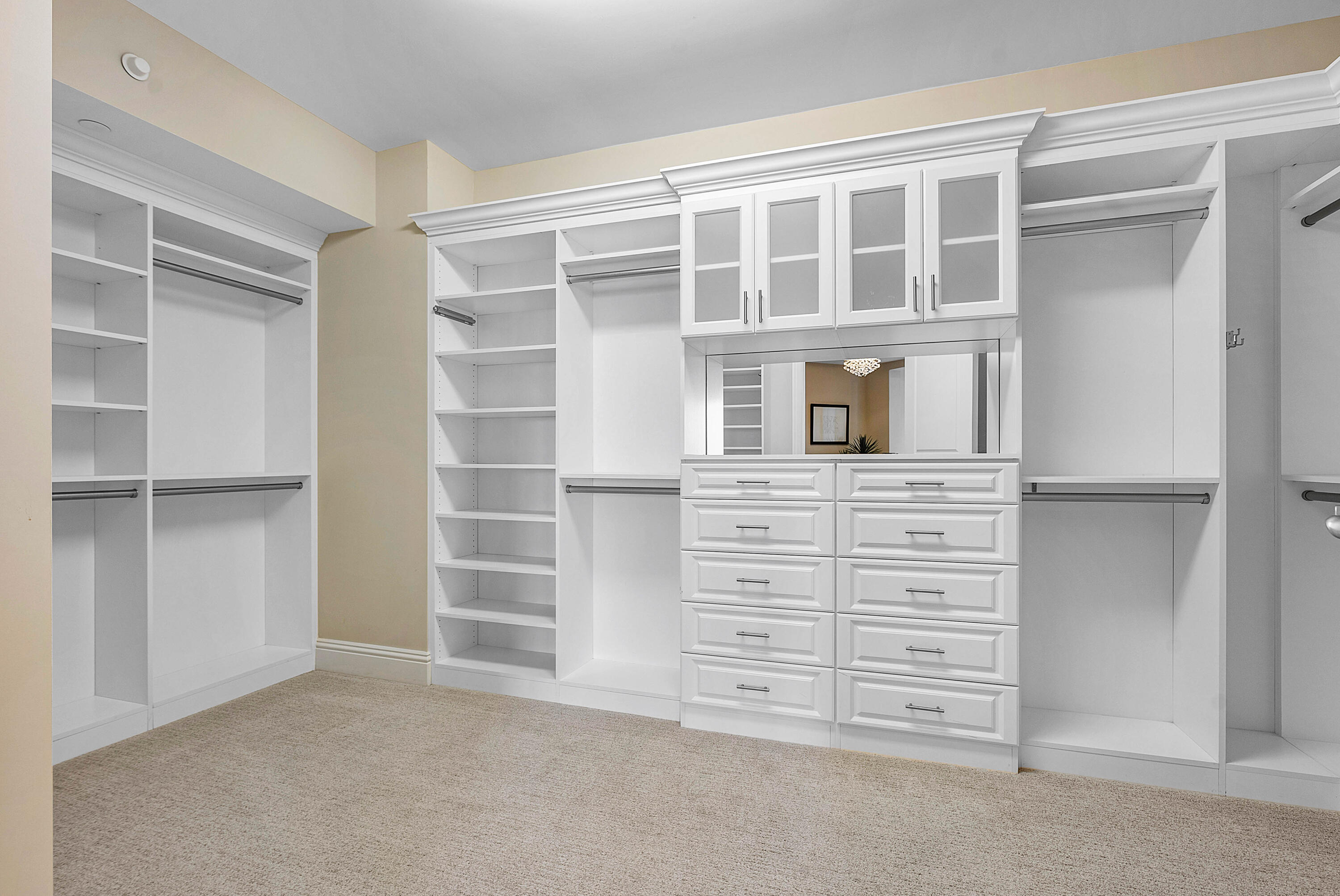 Walk-in closet with white built-in shelves, hanging rails, mirrored cabinets, and a central bank of drawers.