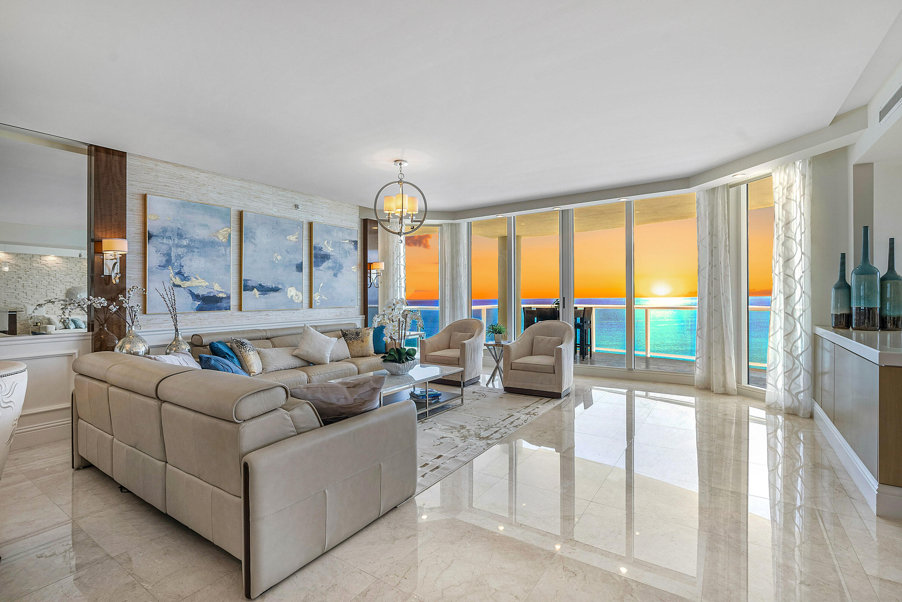 Oceanfront living room with a beige sectional and sunset views through floor-to-ceiling windows.