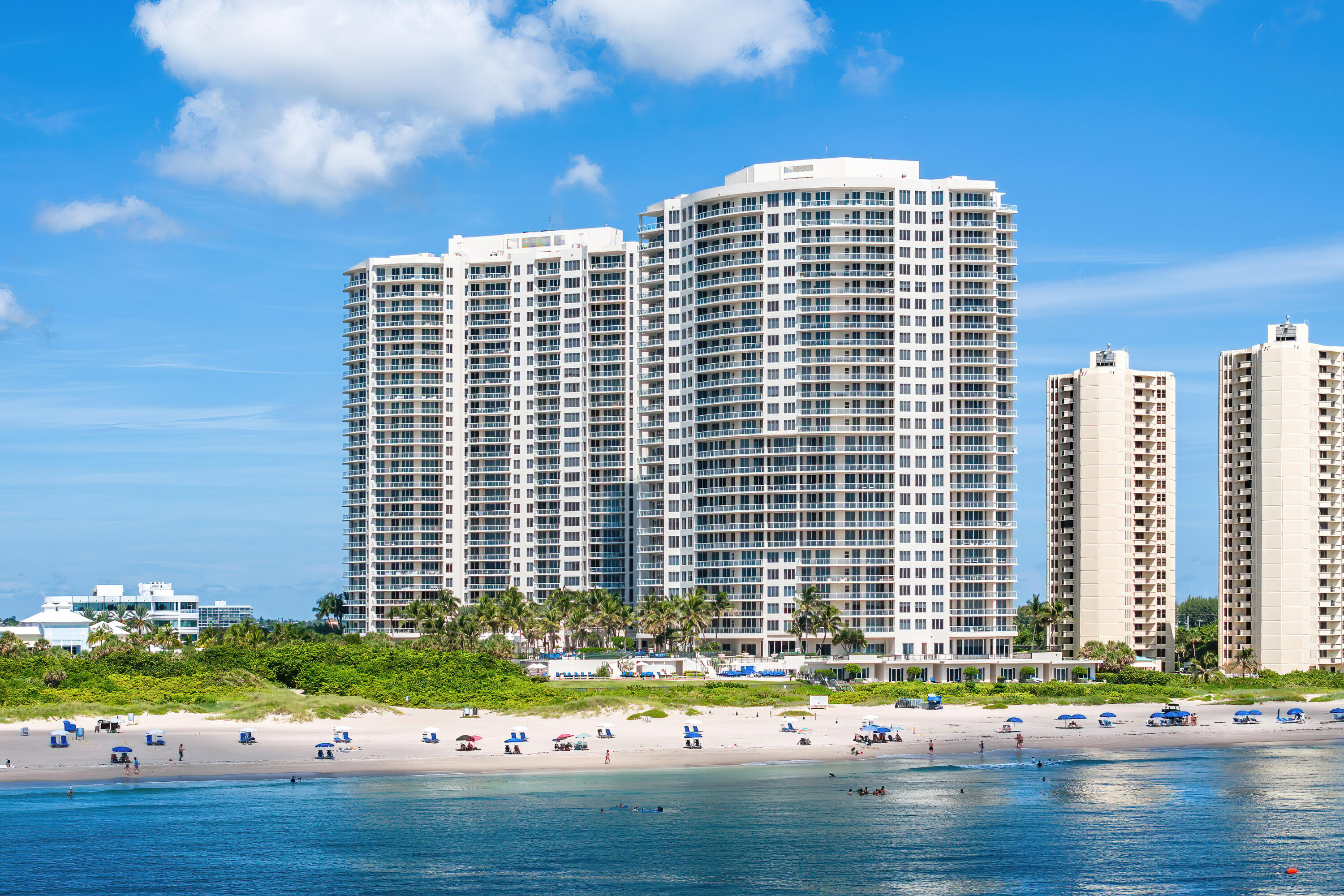 White beachfront condominium towers with curved balconies behind a sandy beach and blue ocean.