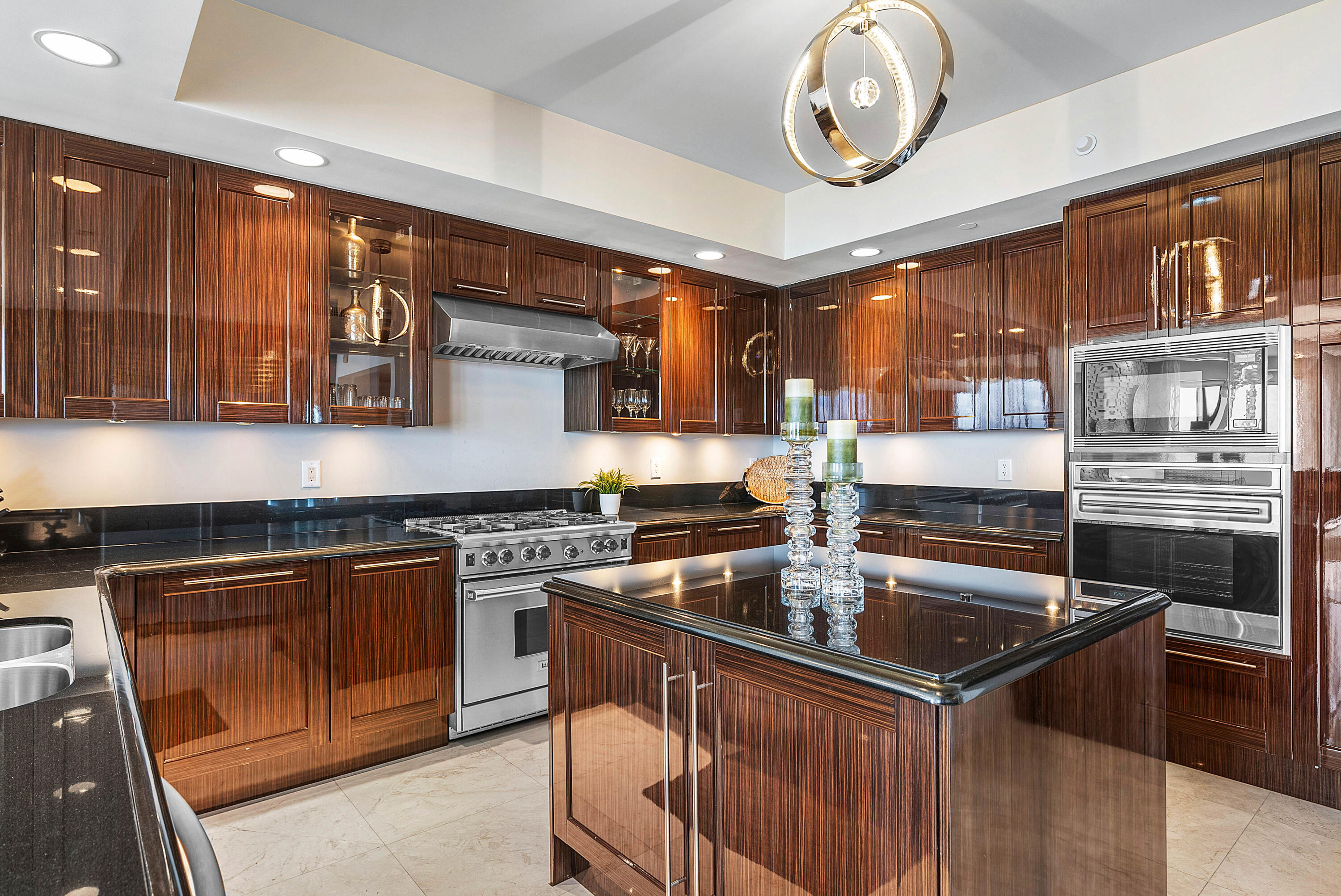 Luxury kitchen with glossy wood cabinets, a large island, black countertops, and stainless steel appliances.