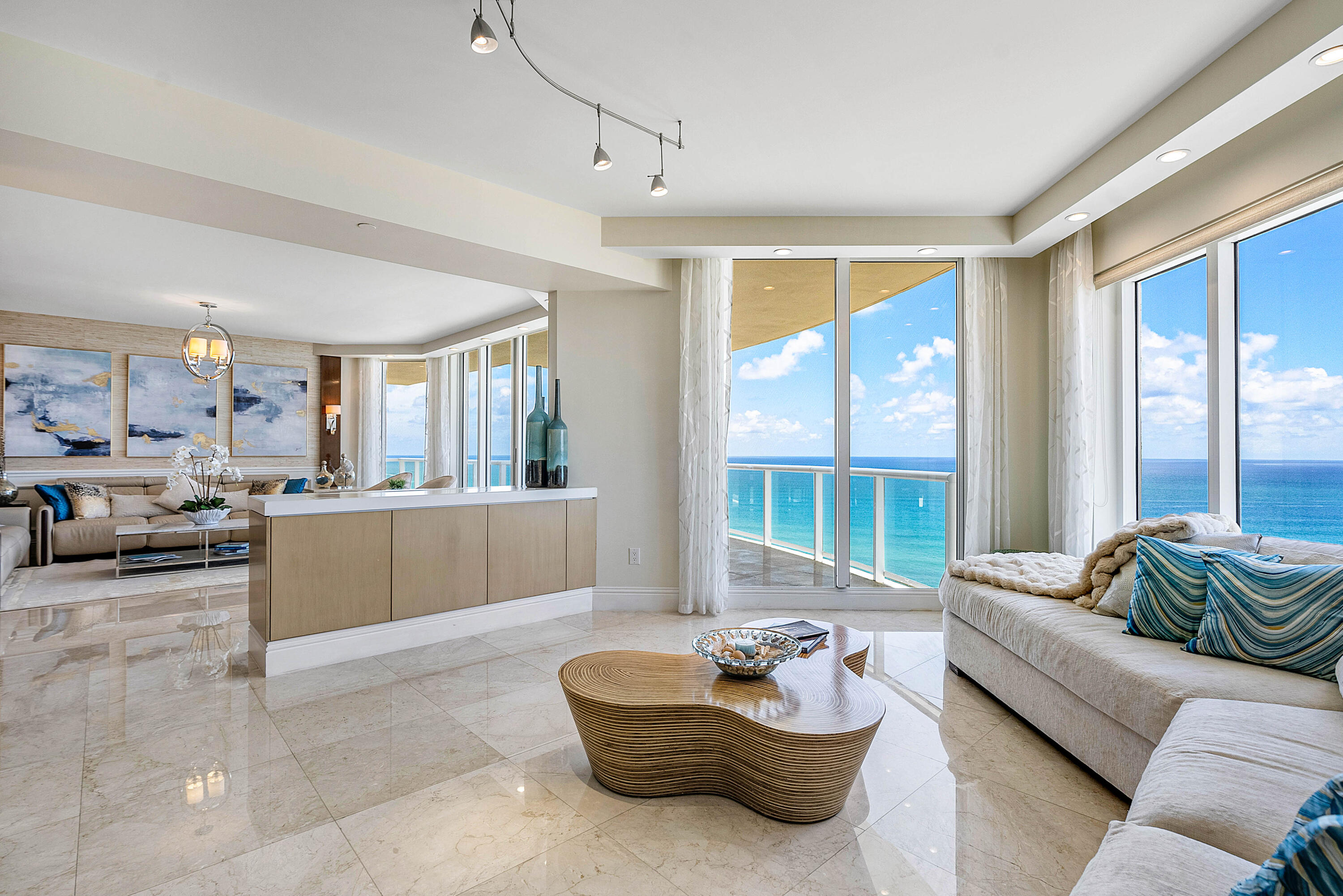 Oceanfront condo living room with cream seating and floor-to-ceiling windows overlooking the water.