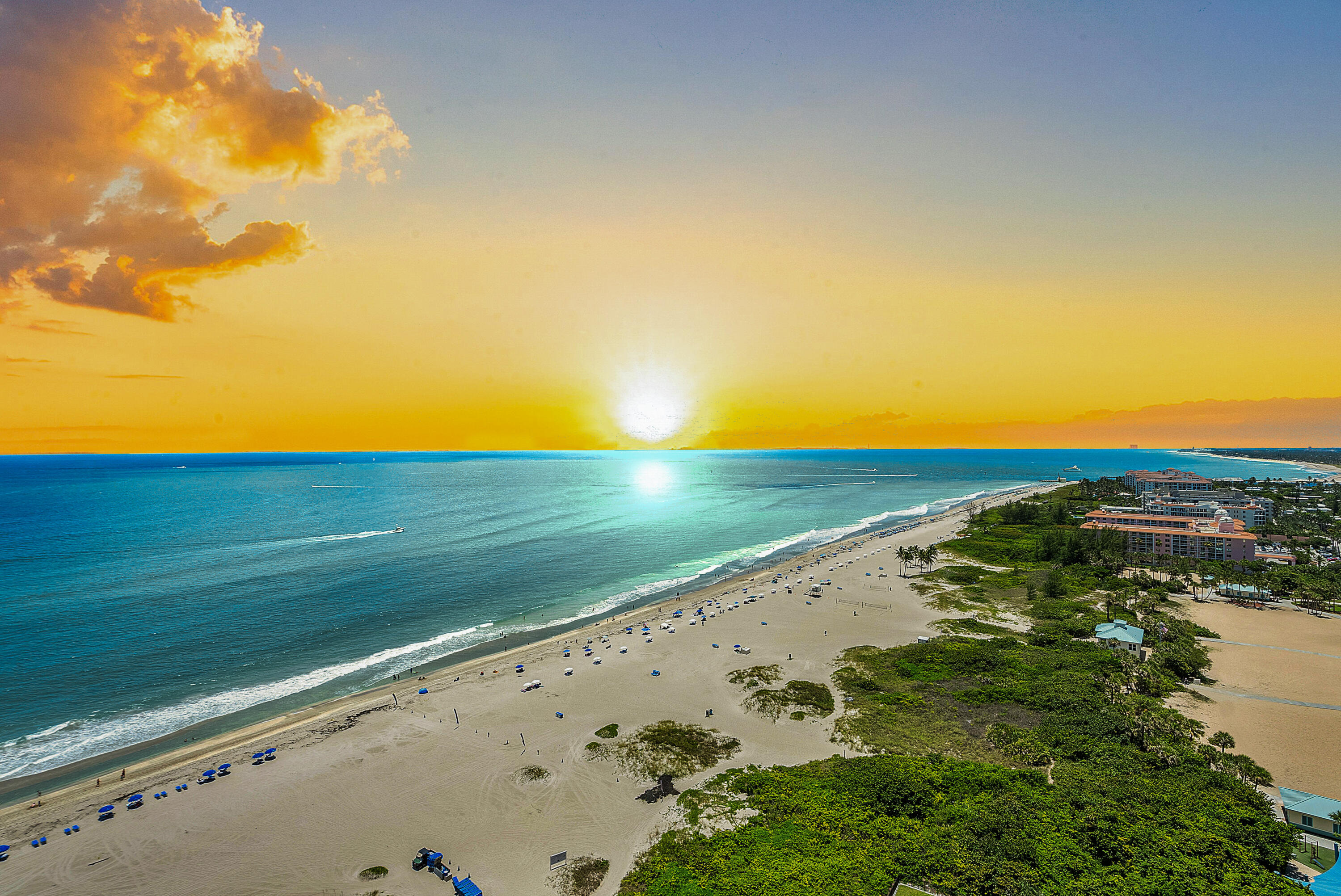 Oceanfront beach and turquoise water at sunset, with beachfront buildings along the shore.