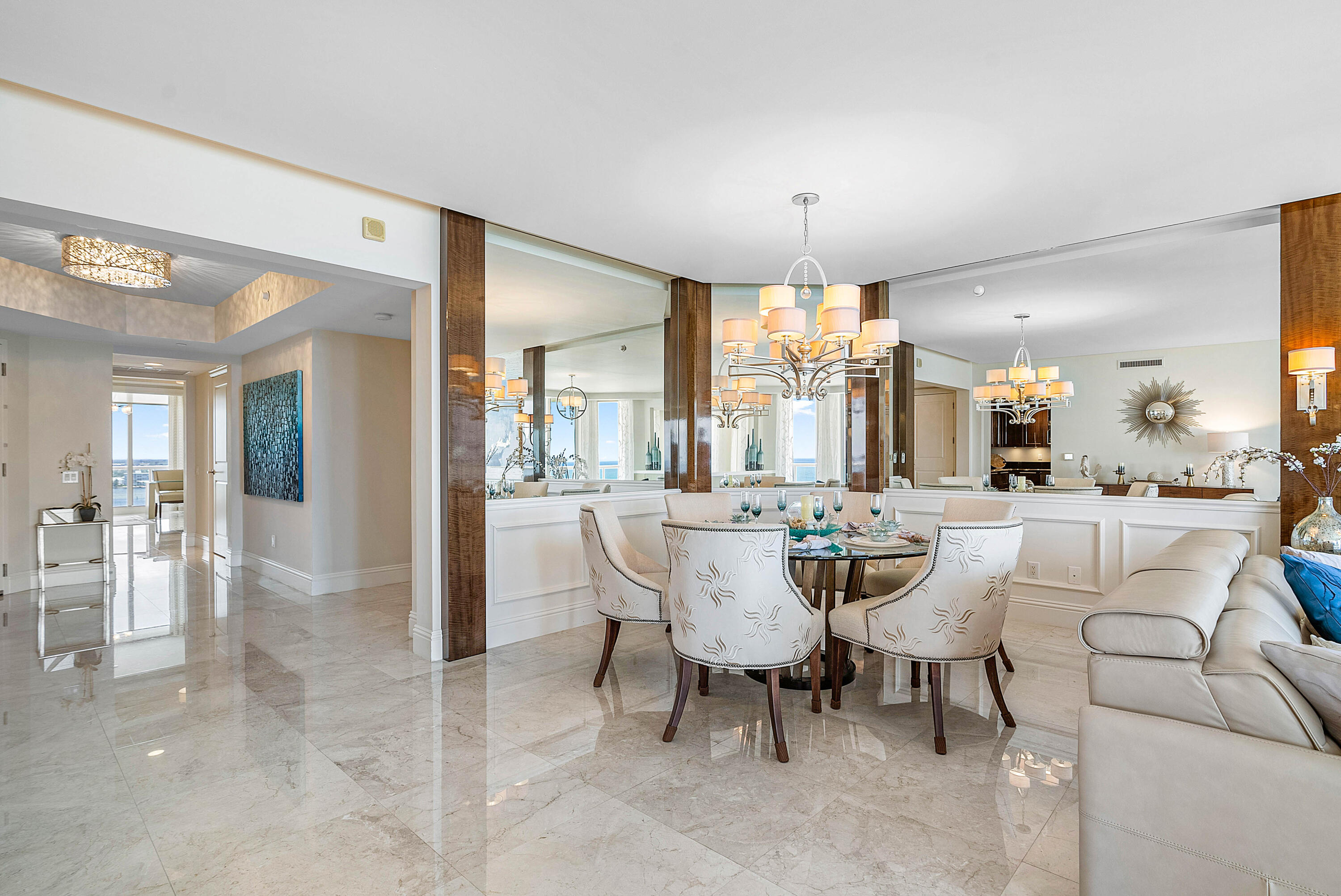 Furnished condo dining room with mirrored walls, a chandelier, marble floors, and ocean views.
