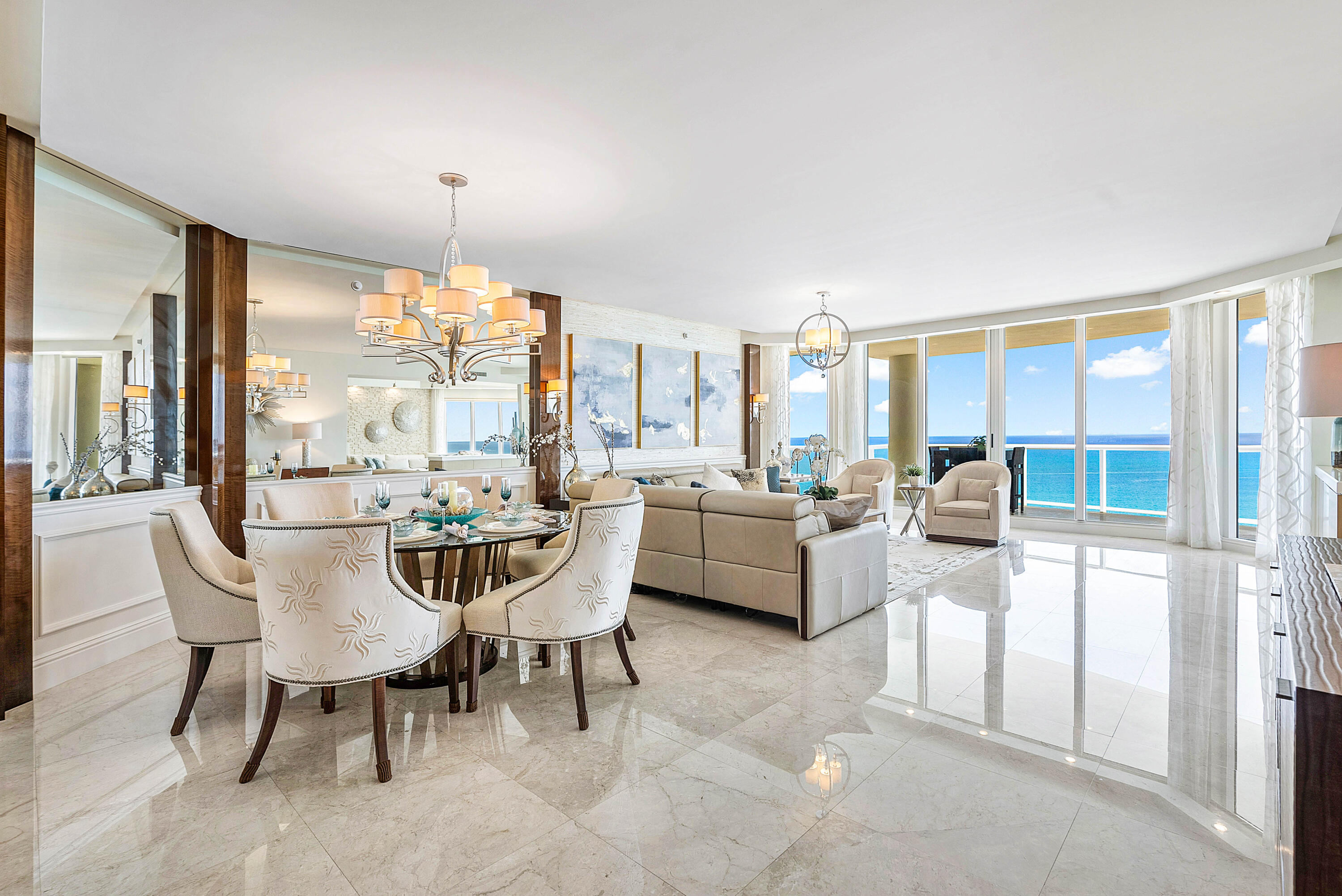 Open-plan living and dining room with cream furnishings and floor-to-ceiling windows overlooking the ocean.