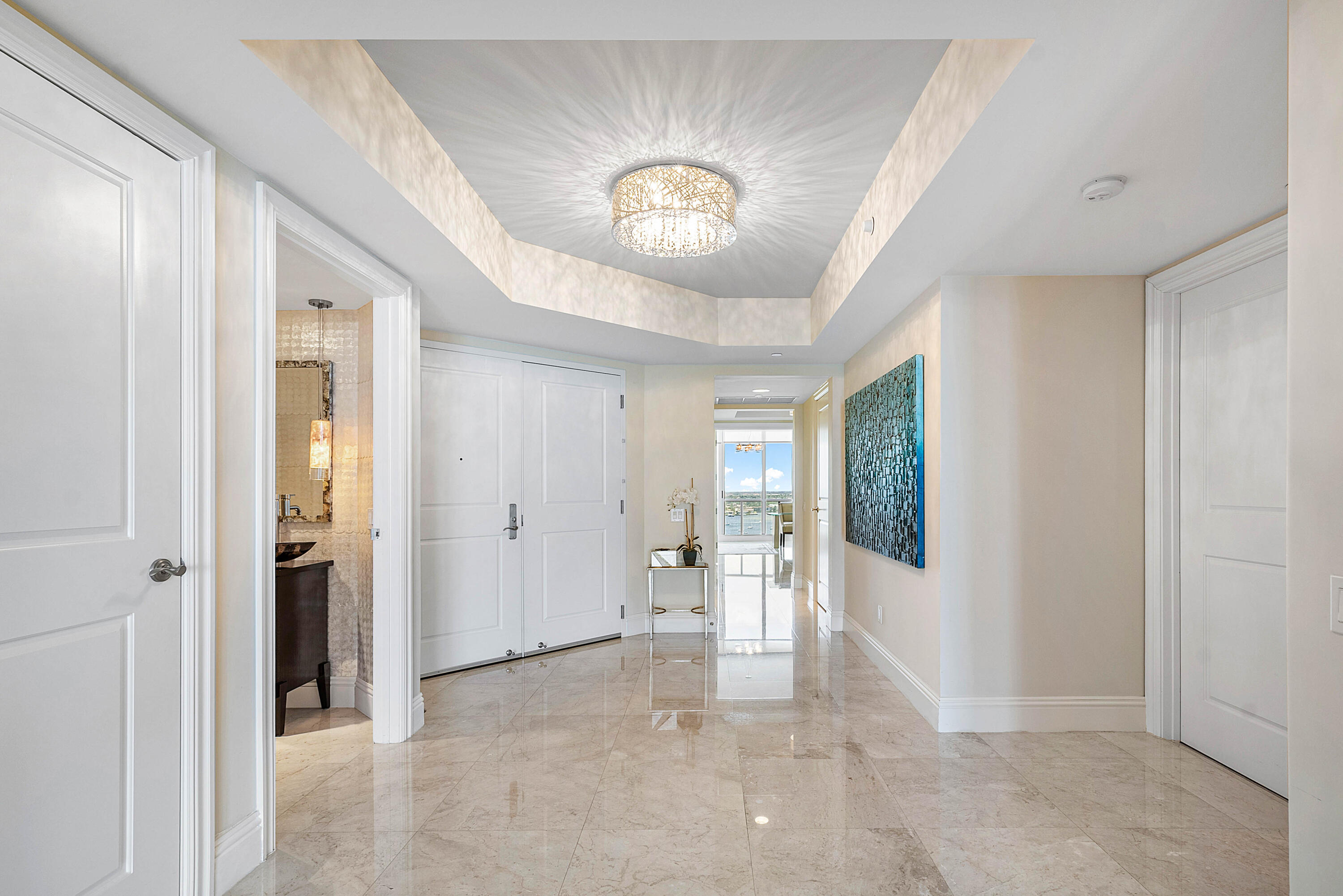 Condominium entry hall with polished marble floors, a tray ceiling chandelier, and a distant water view.