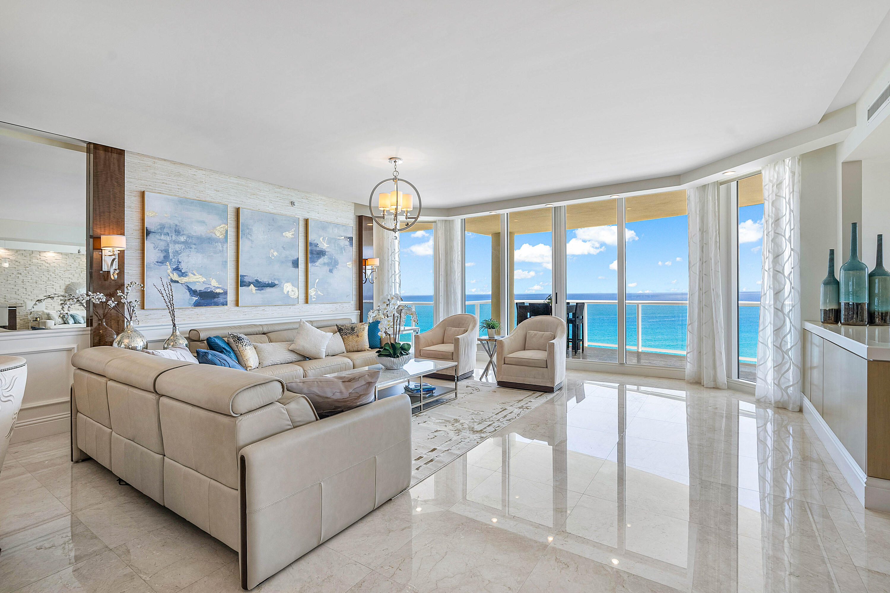 Furnished living room with a cream sectional and floor-to-ceiling windows overlooking the ocean.
