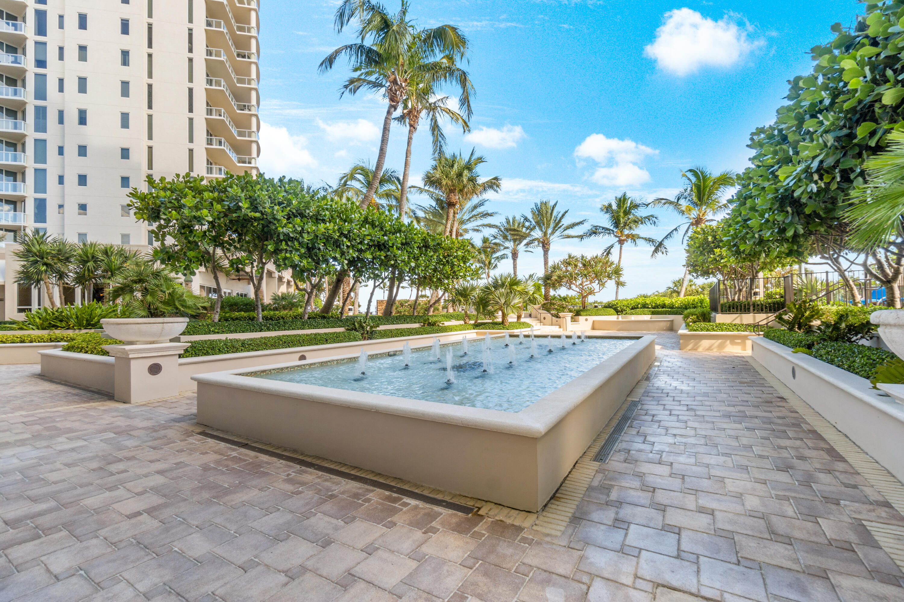 Condominium courtyard fountain pool surrounded by palms, paved walkways, and a high-rise tower.