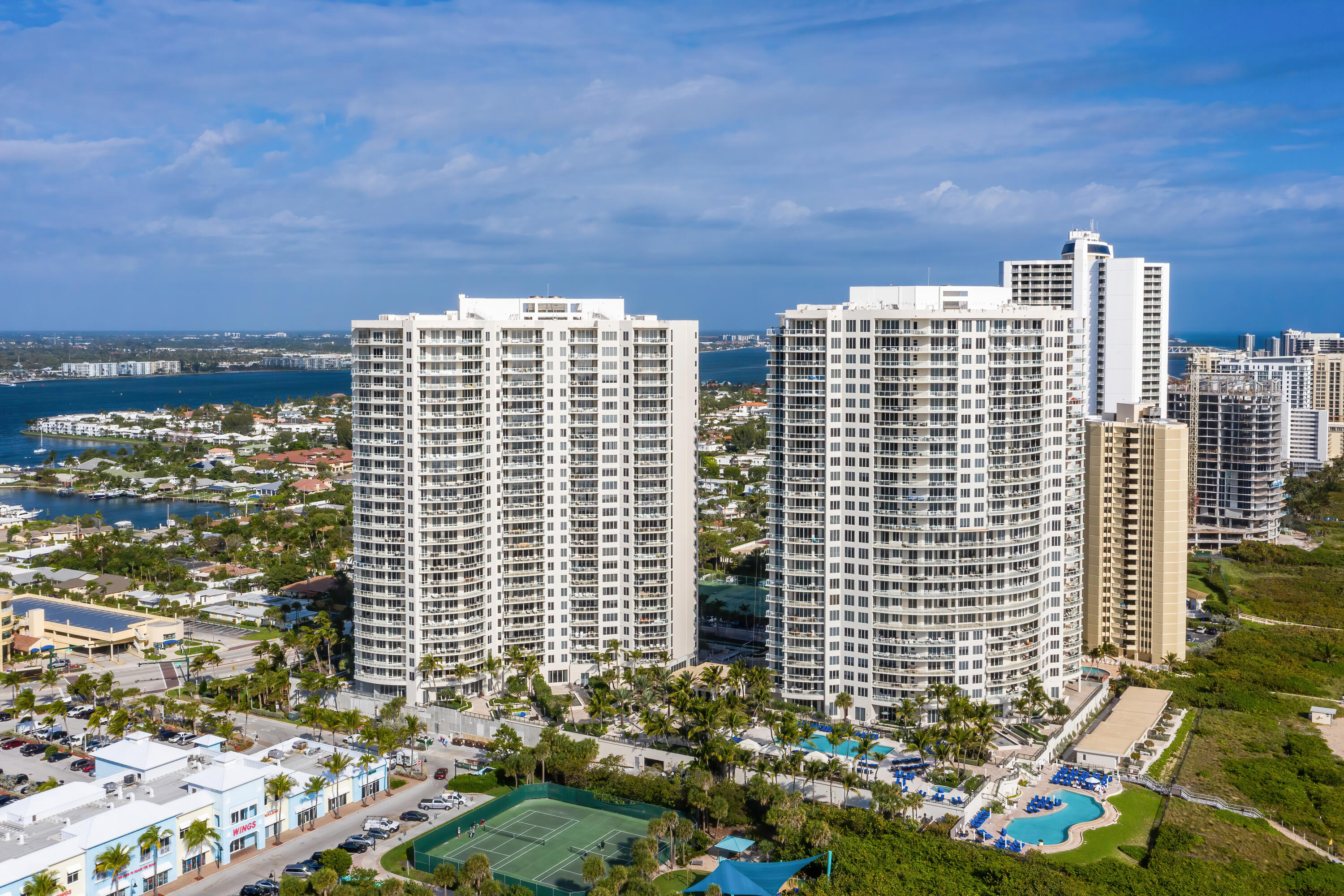 Two white condominium towers beside waterways, with swimming pools and a tennis court.