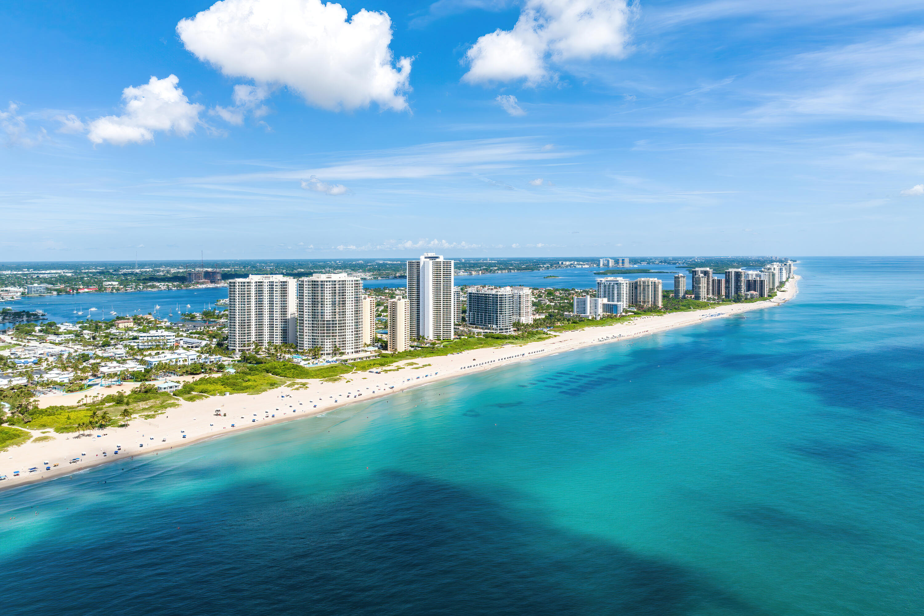 Aerial view of beachfront towers beside a curving white-sand beach and turquoise ocean.