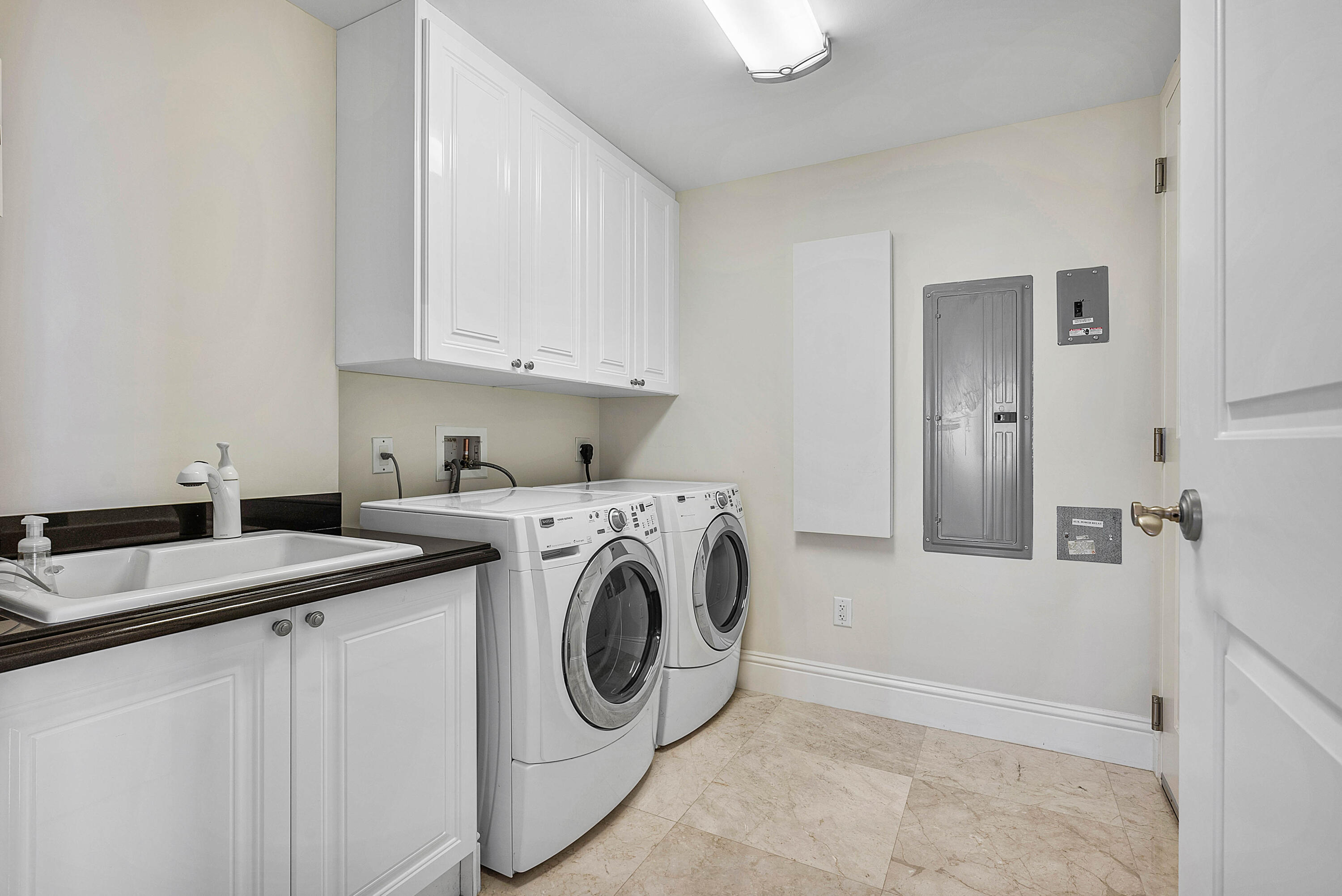 Laundry room with front-loading washer and dryer, utility sink, and white cabinets.