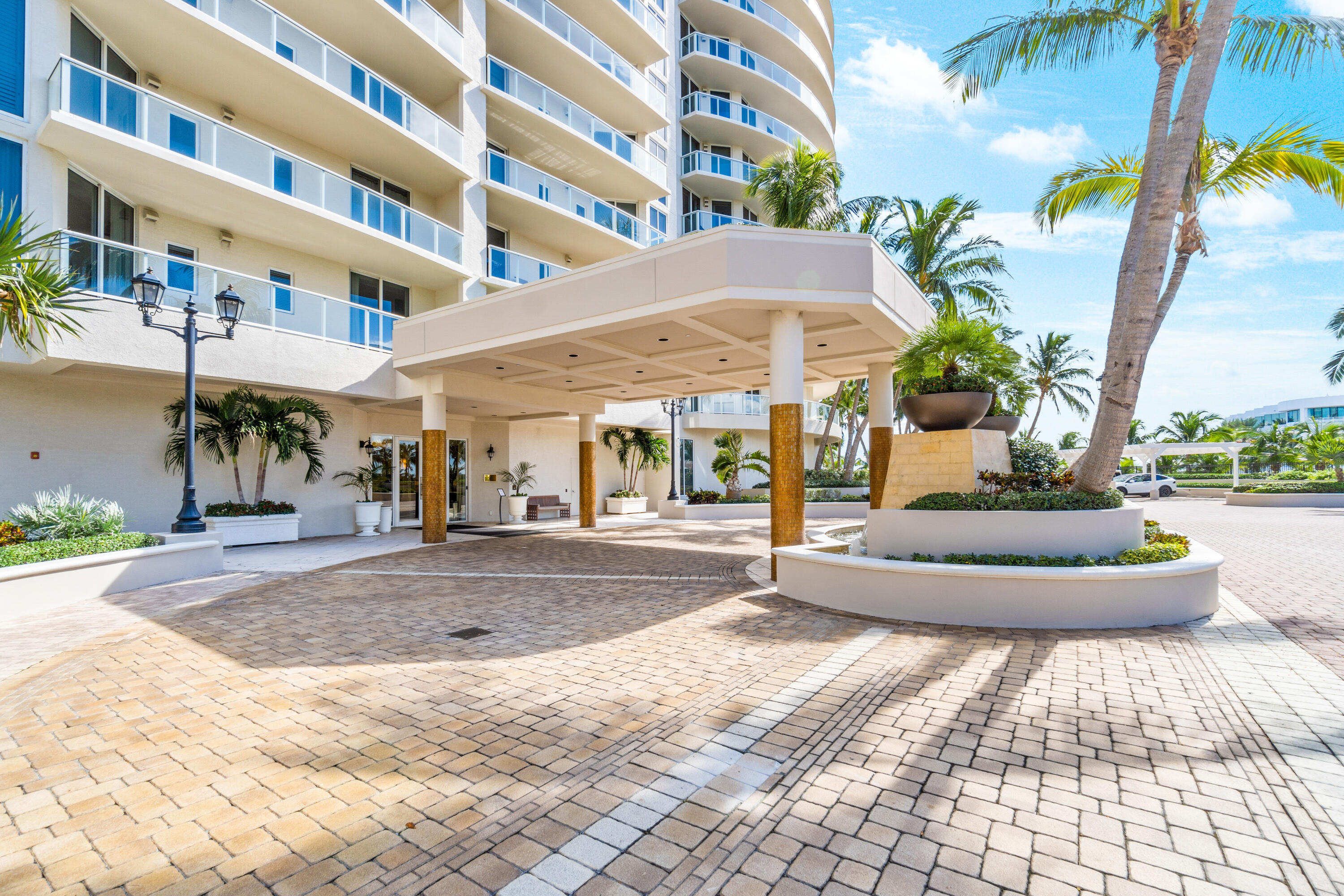 Condominium entrance with a covered porte-cochère, curved balconies, palm trees, and a paved drive court.