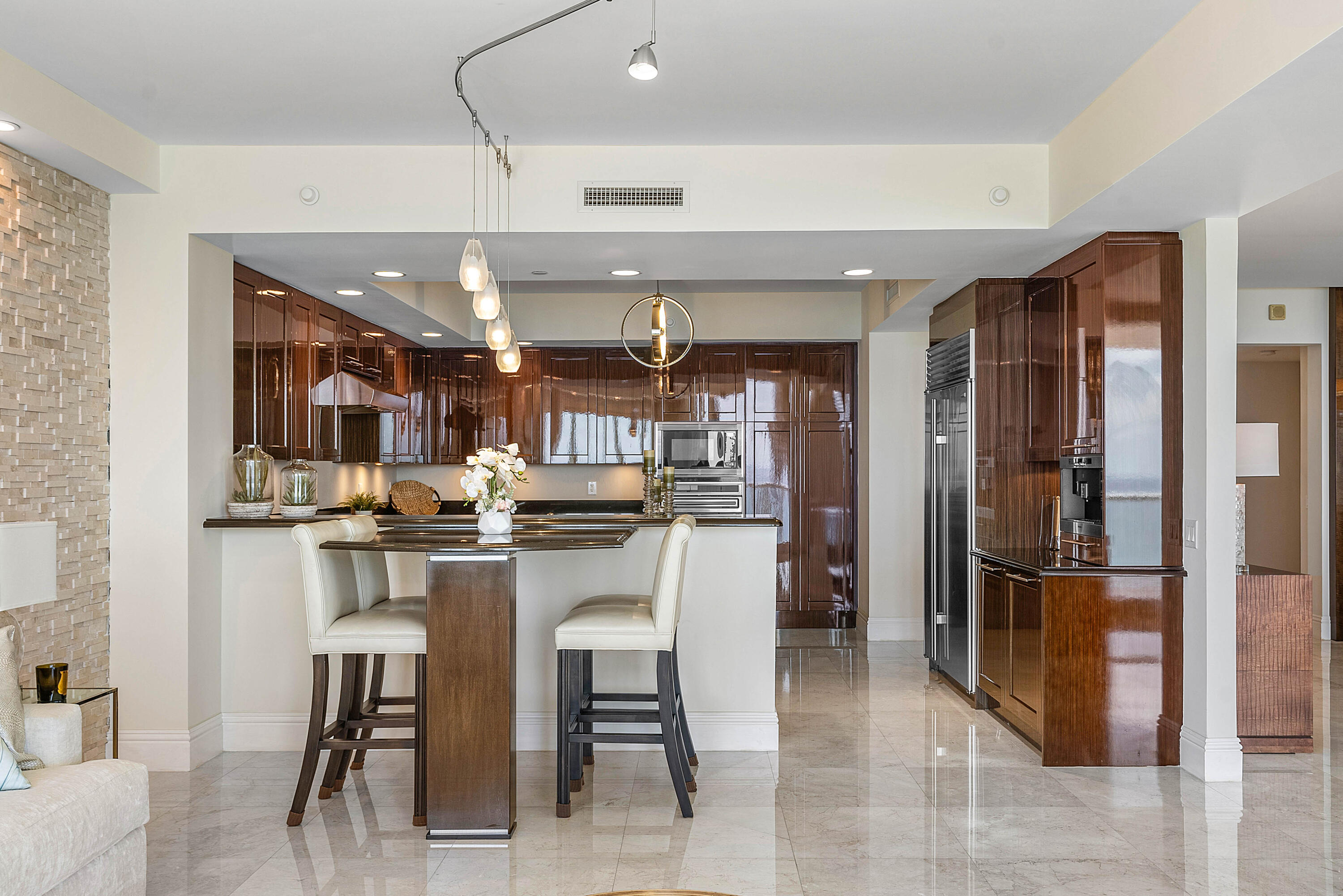 Condominium kitchen with glossy dark wood cabinets, stainless steel appliances, and a breakfast bar.