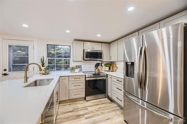 Bright white kitchen with quartz counters, stainless steel appliances, and wood-look flooring.