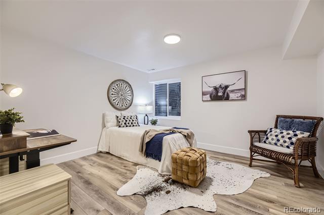 Bedroom with a white bed, woven armchair, and tufted ottoman on a hide rug.
