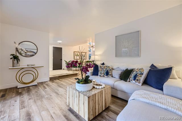 Staged living room with a white sectional, blue accent pillows, and flowers on a wood coffee table.