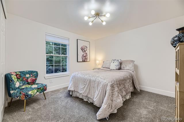 Bedroom with pale patterned bedding, a floral accent chair, and a window.