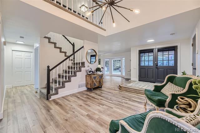 Two-story foyer with a dark staircase, black double entry doors, and green upholstered chairs.