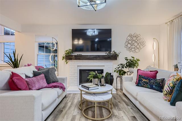 Living room with white sofas, colorful pillows, and a white brick fireplace beneath a television.