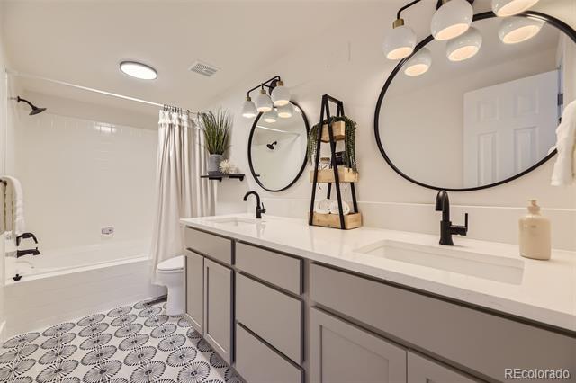 Bathroom with a double vanity, black fixtures, oval mirrors, and patterned tile flooring.