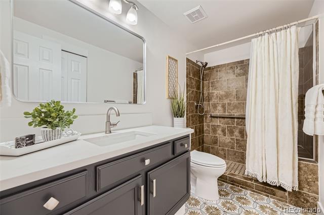 Bathroom with a dark gray vanity, brown tile shower, white curtain, and patterned floor tile.