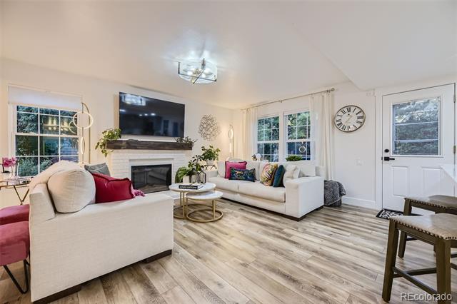Living room with white sofas, a fireplace and television, large windows, and light wood-look flooring.