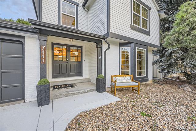 Two-story gray home with dark double front doors, a curved walkway, planters, and a wooden bench.