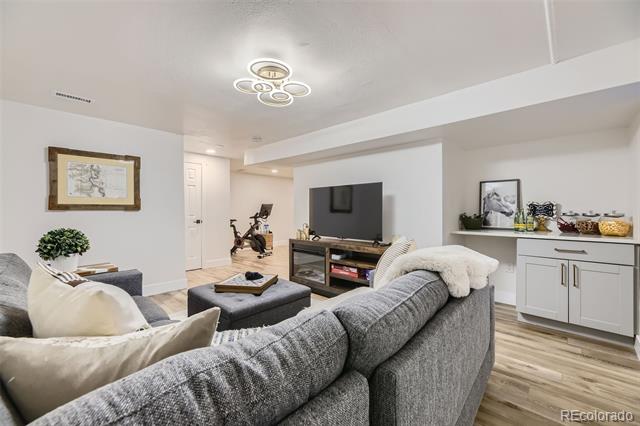 Lower-level living room with a gray sectional, television, exercise bike, and white wet bar.