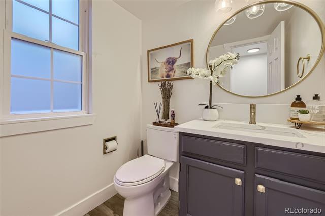 Bathroom with a dark gray vanity, large round mirror, and window beside the toilet.