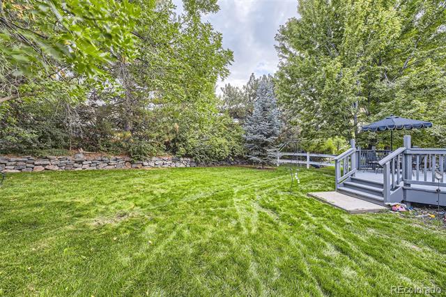 Backyard with a broad green lawn, mature trees, and a raised deck with a blue canopy.